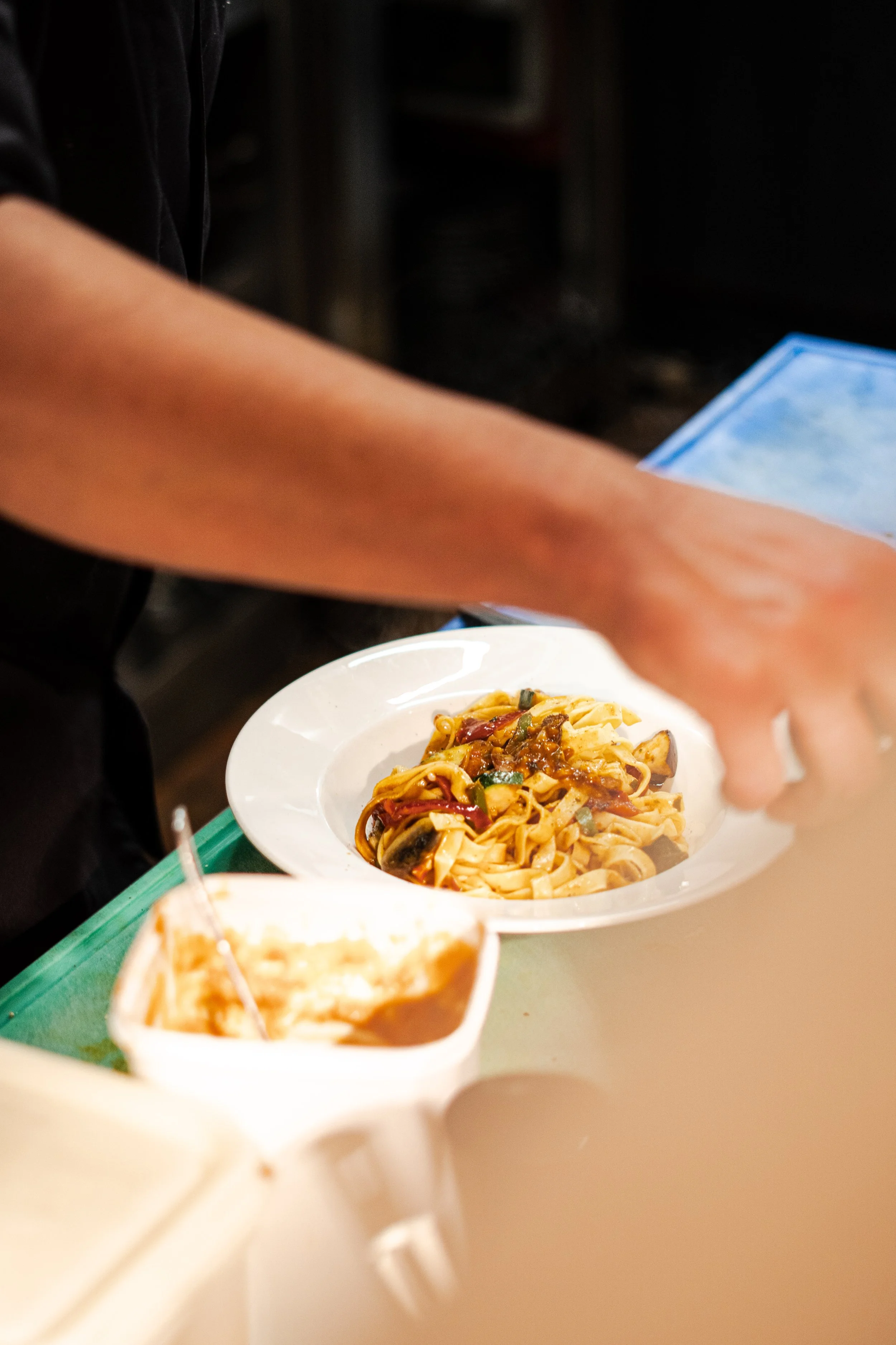 Person serving pasta at a buffet table with other dishes nearby.