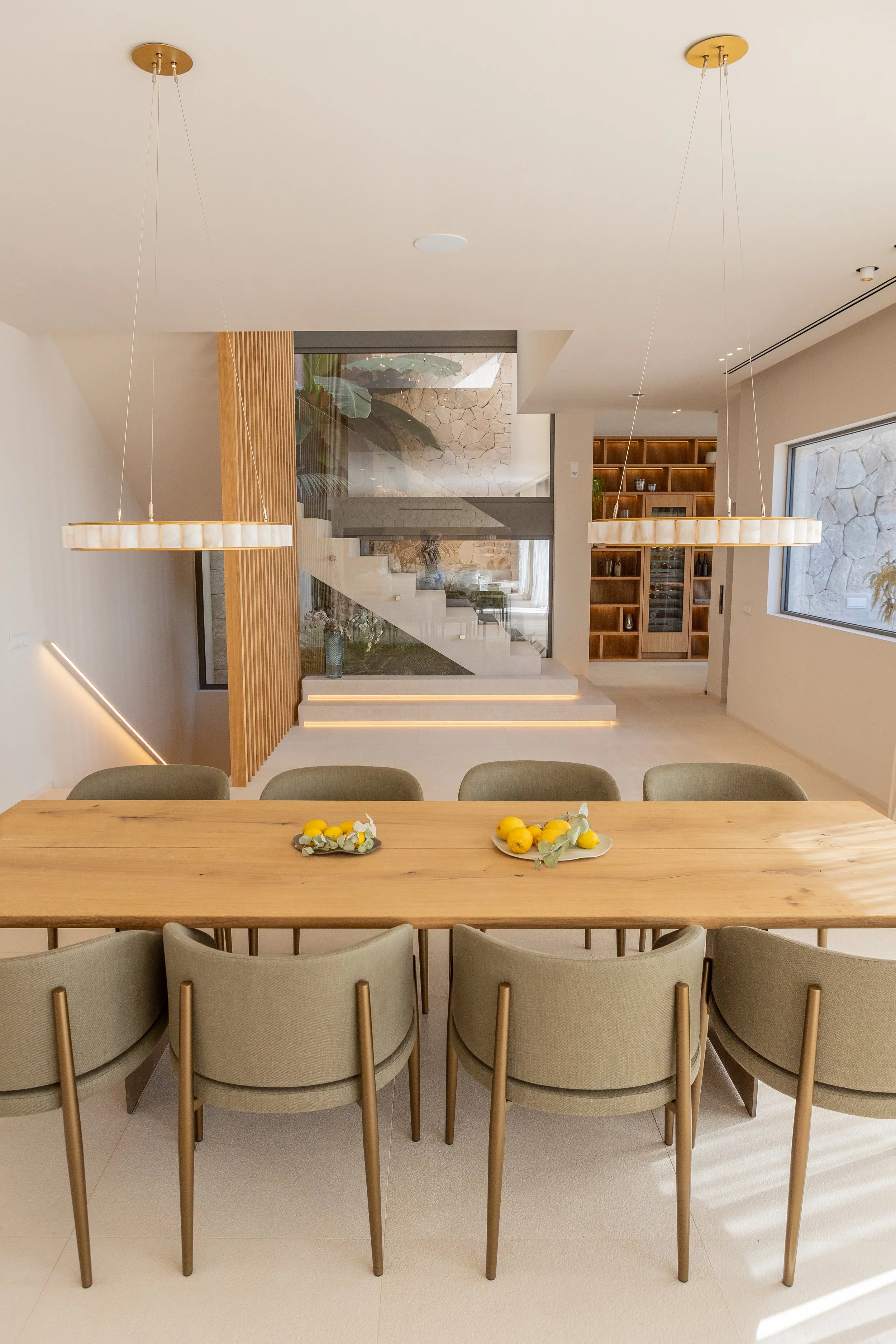 Mesa de madera con seis sillas grises y dos platos con limones y flores blancas y verdes.