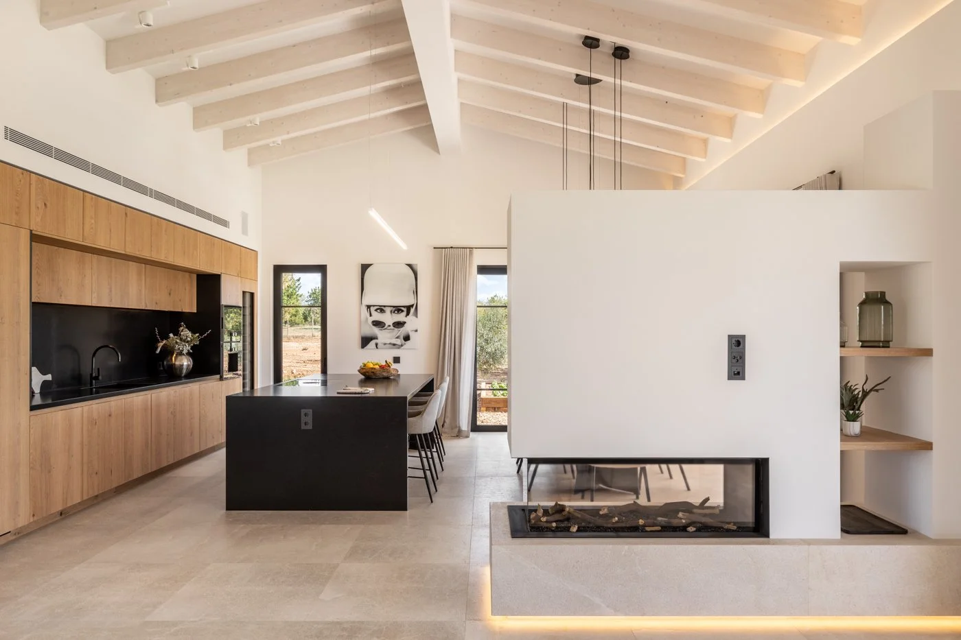 Interior de una sala de diseño moderno con techo de vigas blancas, pared de madera, isla de cocina negra, y chimenea decorativa.
