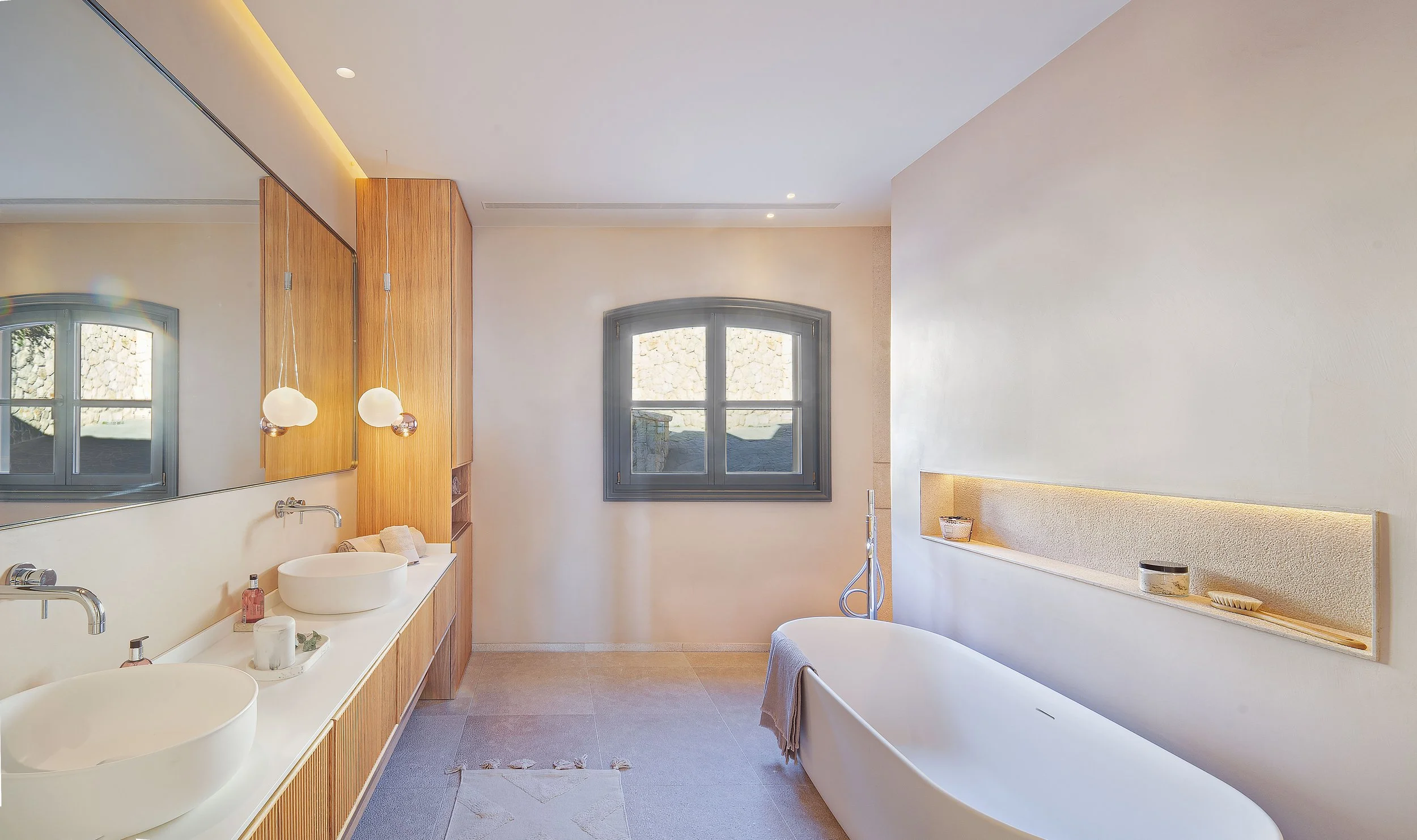 Interior de un baño moderno con una tina, dos ventanas, y un espejo grande.
