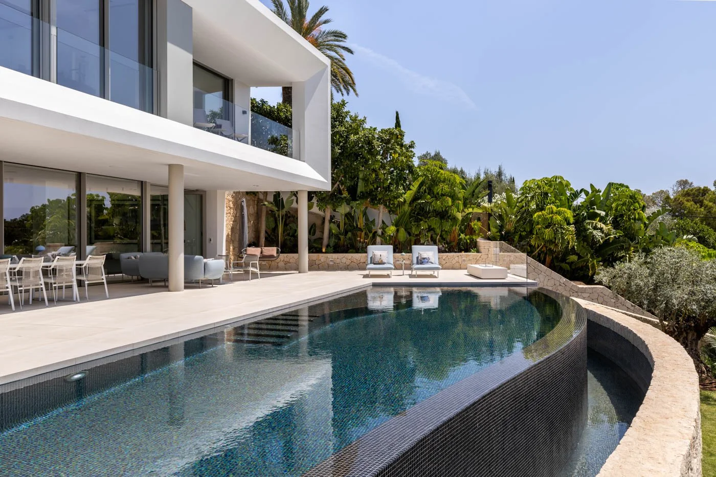 Vista de una casa moderna con piscina en el patio trasero, rodeada de vegetación y muebles de exterior.