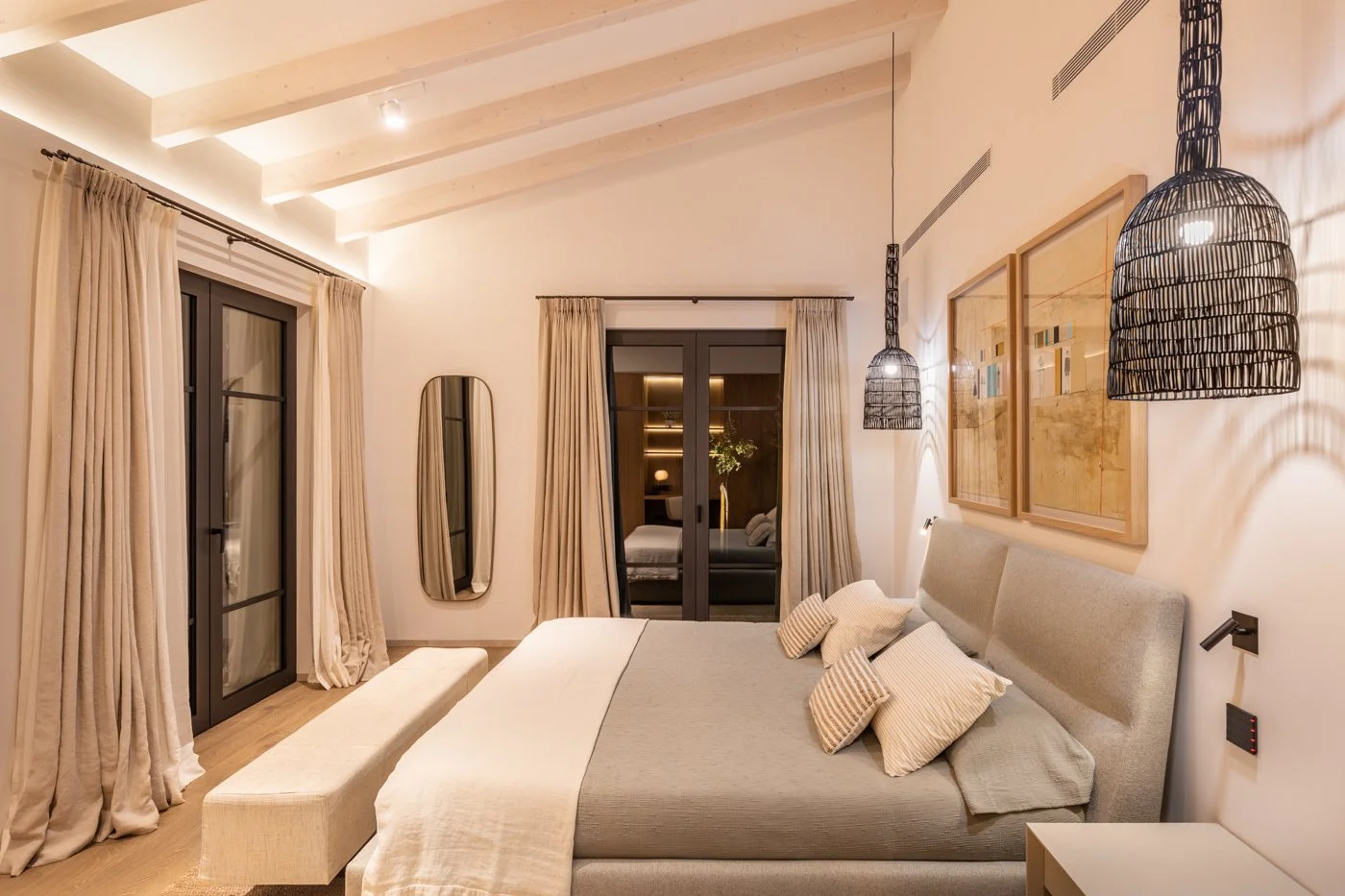 Habitación moderna con cama grande, cojines, cortinas beige, lámparas de mimbre colgantes, cuadros en la pared y espejo