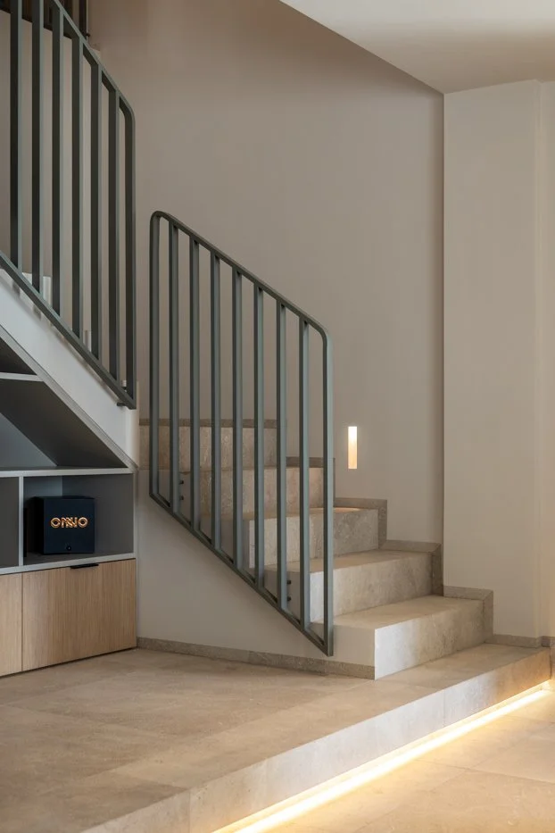 Escalera interior de cemento con barandilla de metal en un espacio moderno, con iluminación empotrada en el suelo.