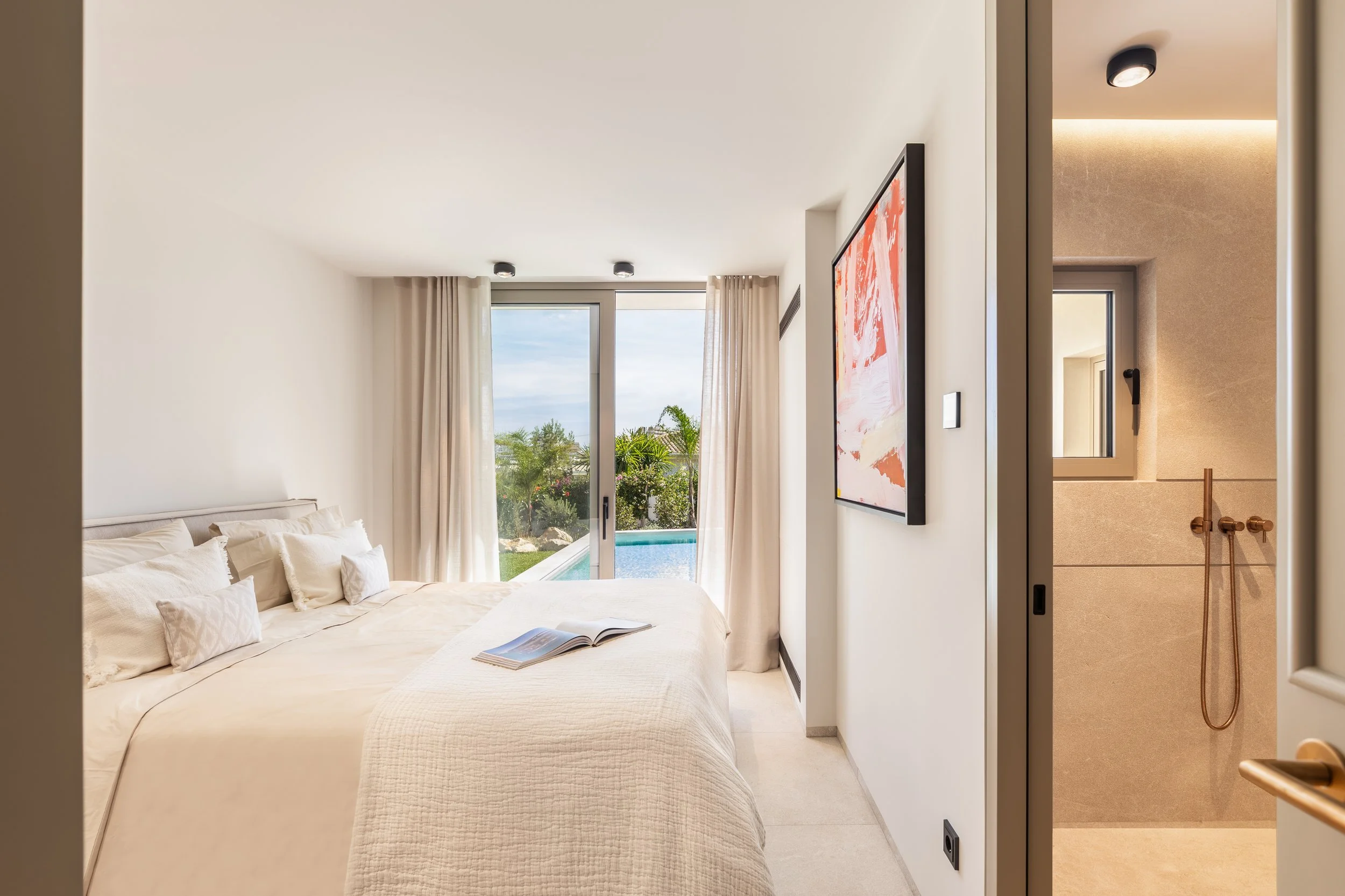 Habitación moderna con cama blanca, ventana grande con cortinas claras y vista a un jardín y piscina, decoración minimalista, espacio luminoso y ordenado.