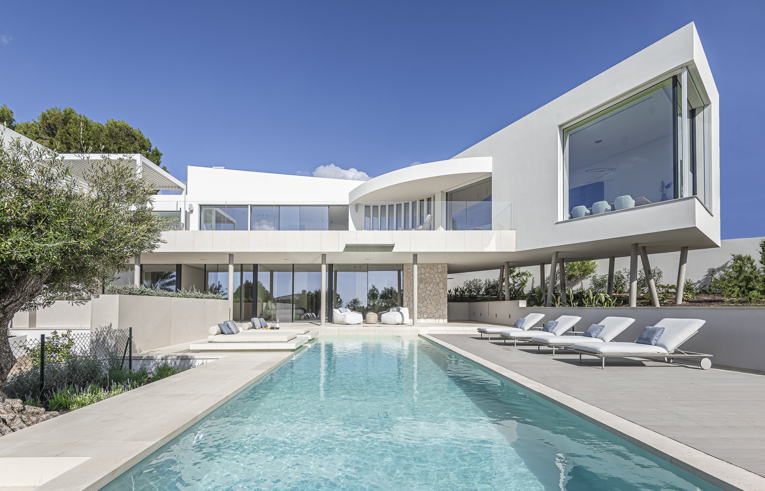 Casa moderna blanca con piscina y tumbonas en un entorno soleado y despejado.