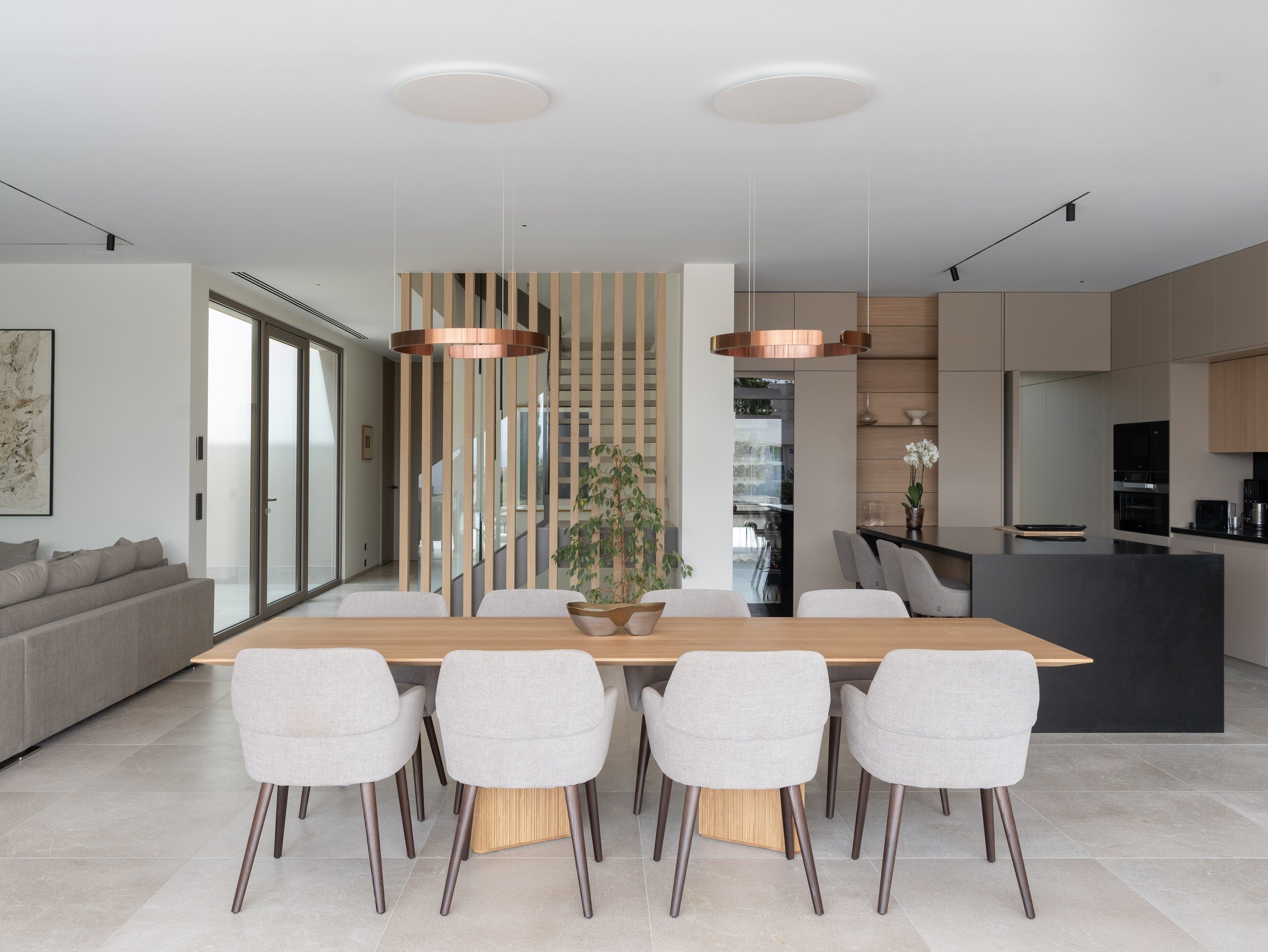 Comedor con mesa de madera y sillas blancas. Cocina moderna con gabinetes en beige y electrodomésticos integrados. Decoración minimalista con plantas y obras de arte.