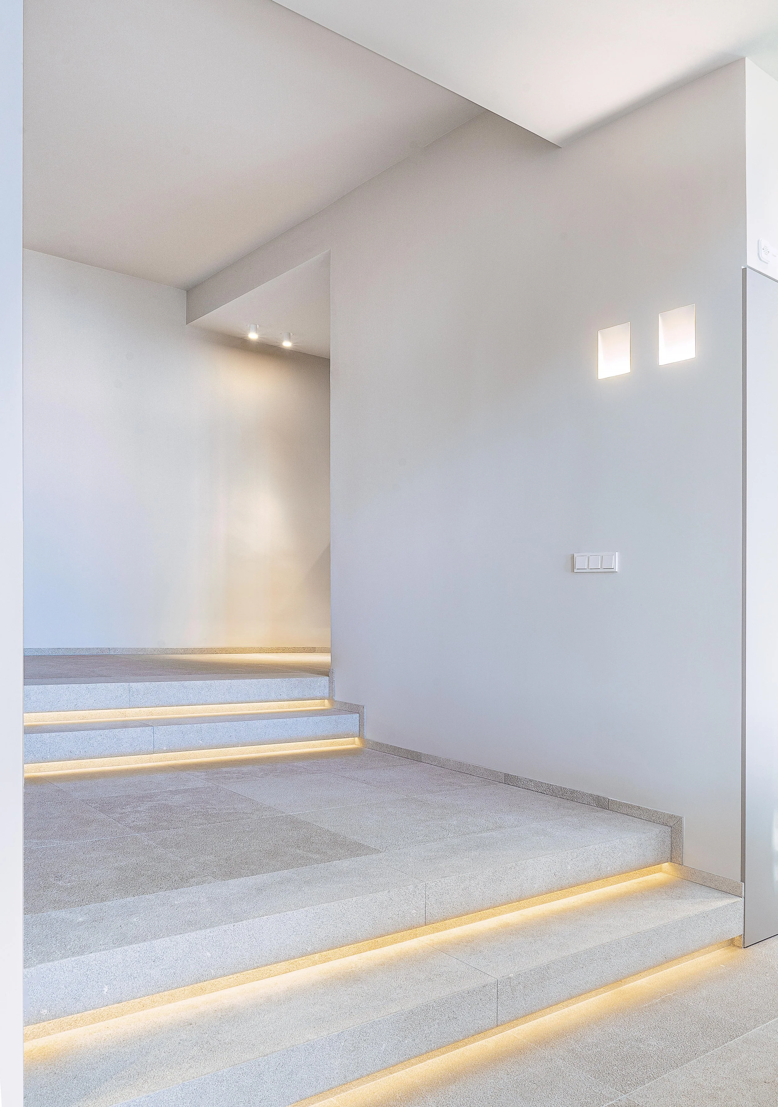 Escalones de escaleras en un espacio interior moderno con iluminación suave y paredes blancas.