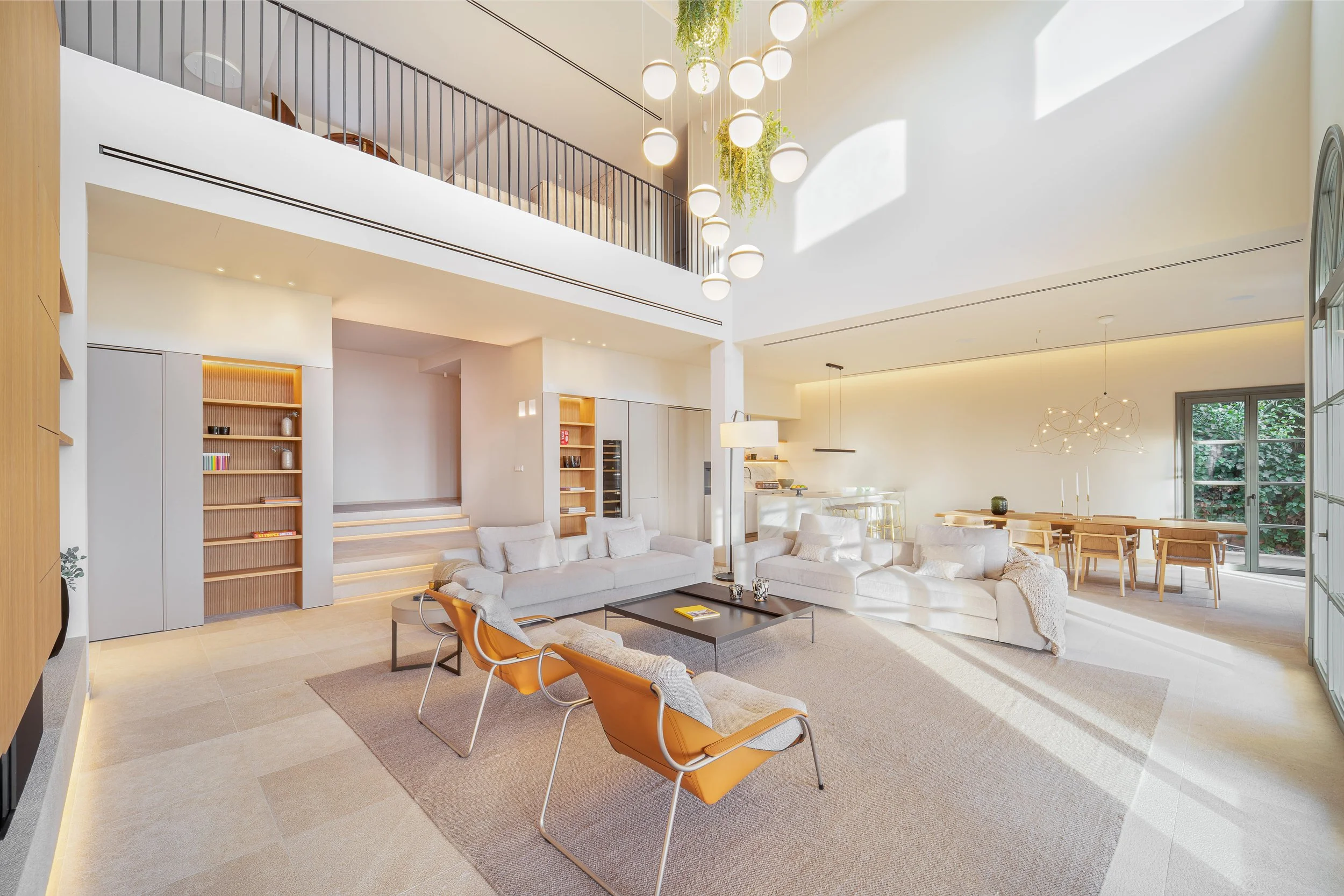 Sala de estar moderna y luminosa con sillones blancos, mesas de centro negras, lámparas colgantes y ventanas grandes que dejan entrar luz natural.