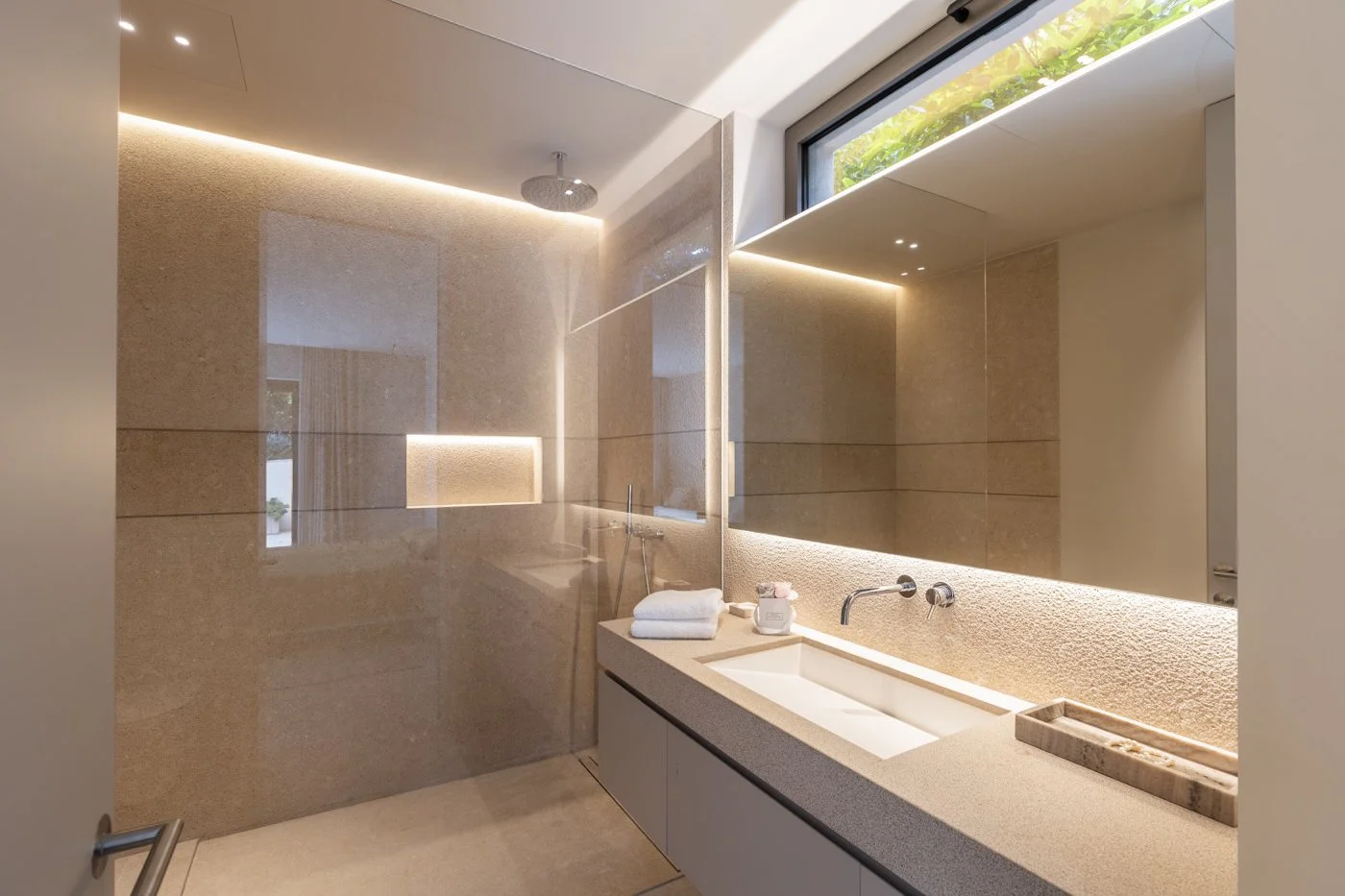 Baño moderno con lavabo en encimera, espejo grande, iluminación Led, ducha con cabezal redondo y pared de azulejos beige