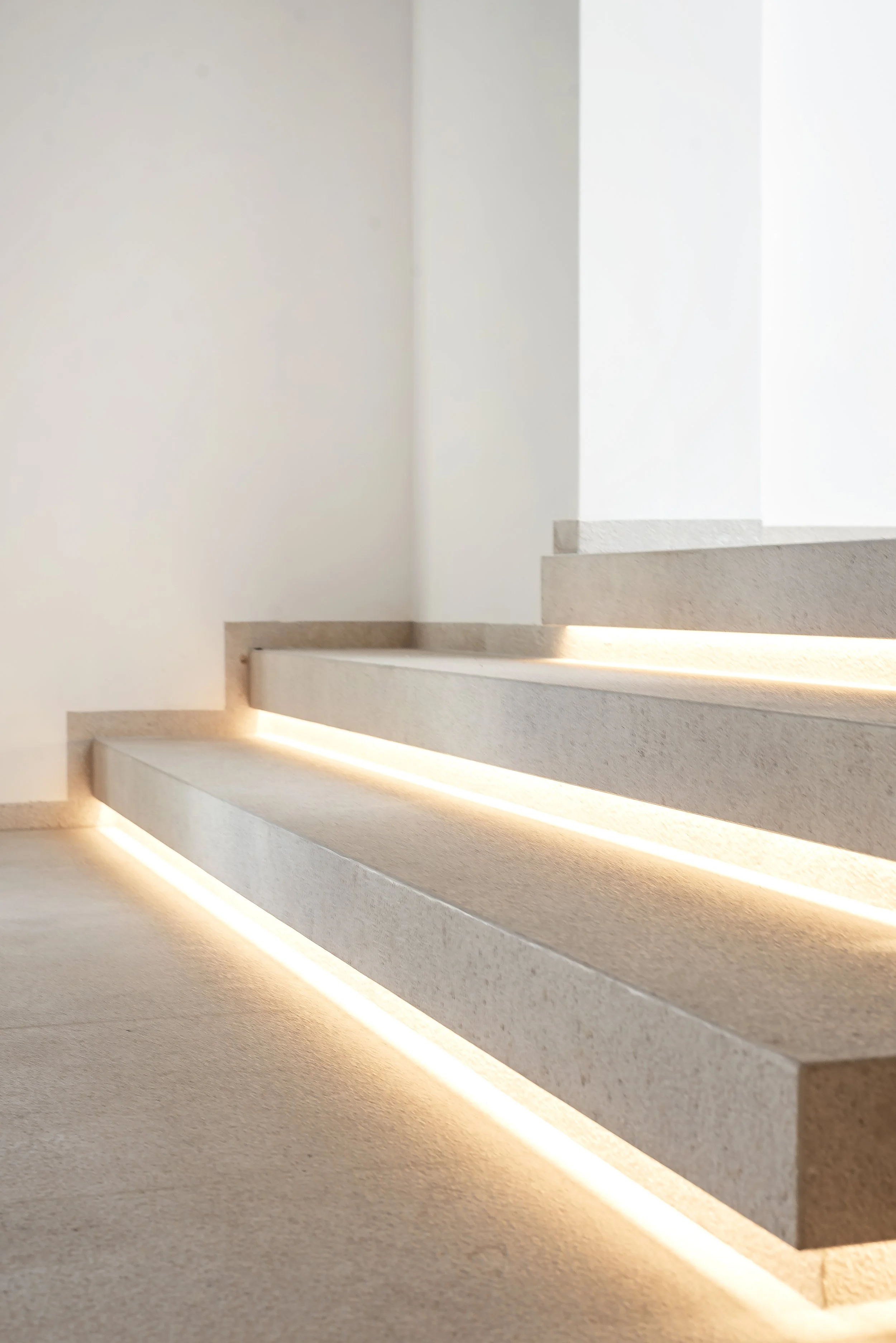 Escalones de piedra con iluminación LED en su base, en una pared blanca