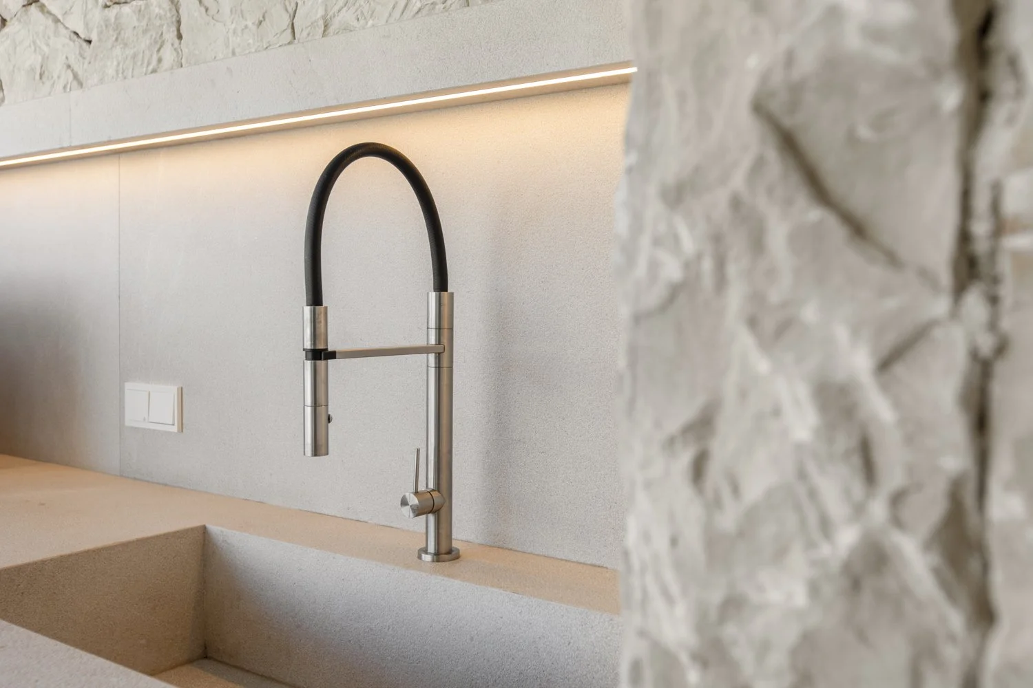 Una llave de cocina moderna en un fregadero de piedra y una pared con decoración de piedra.