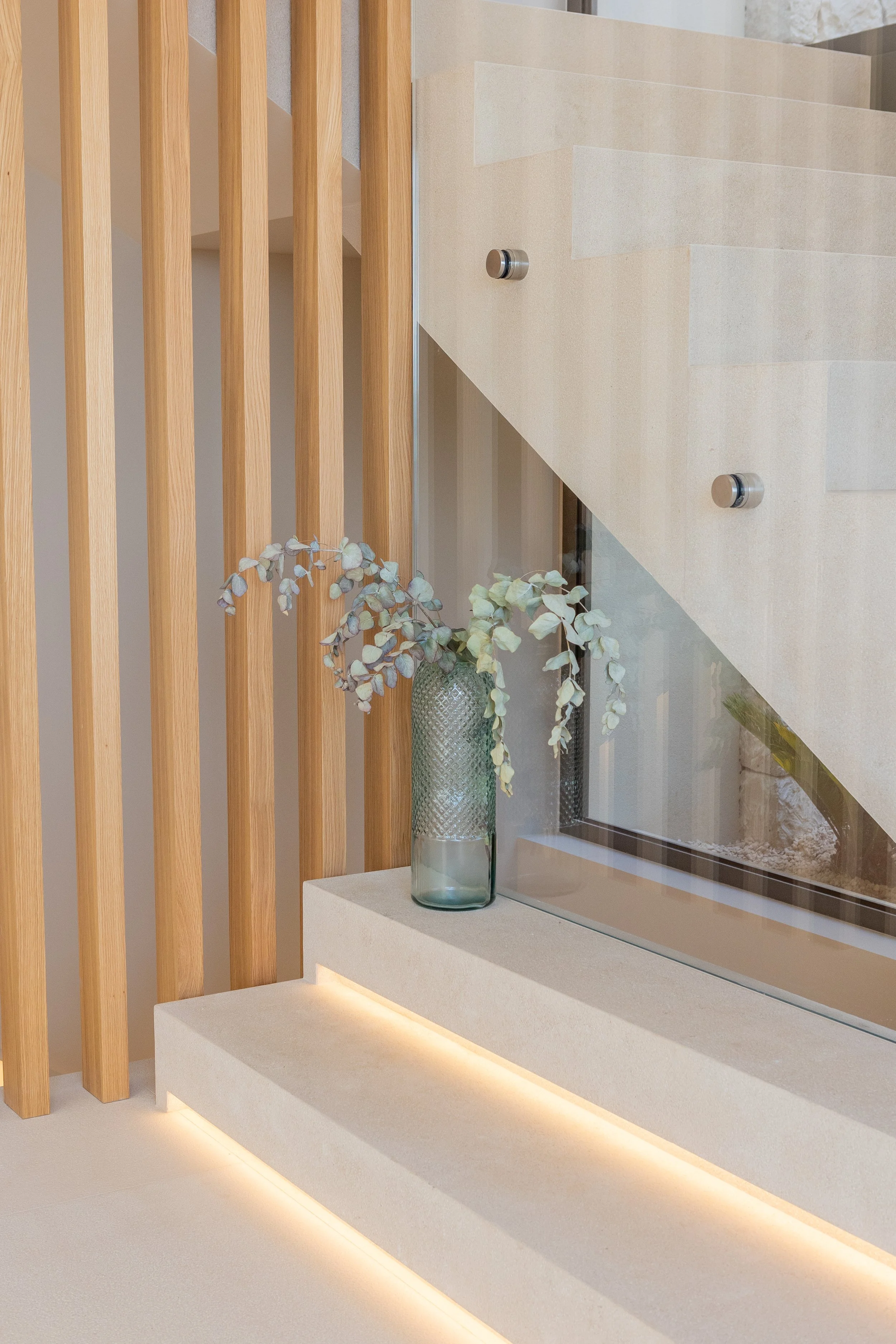 Interior moderno con pared de madera y ventana con vista a un jardín, decorado con un florero de vidrio verde con plantas