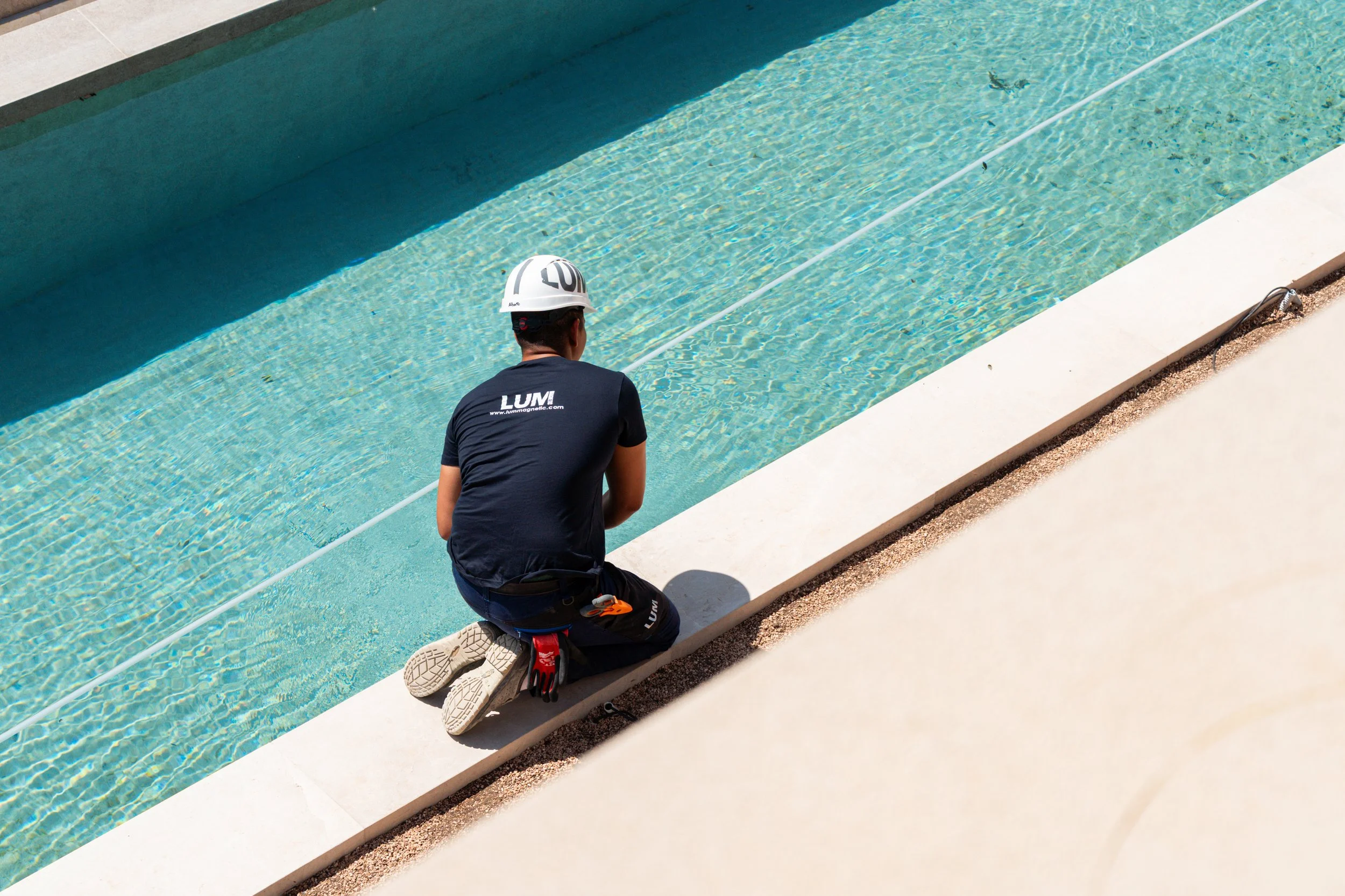 Una persona con casco y equipo de protección trabaja junto a una piscina con agua cristalina, probablemente en una construcción o mantenimiento.