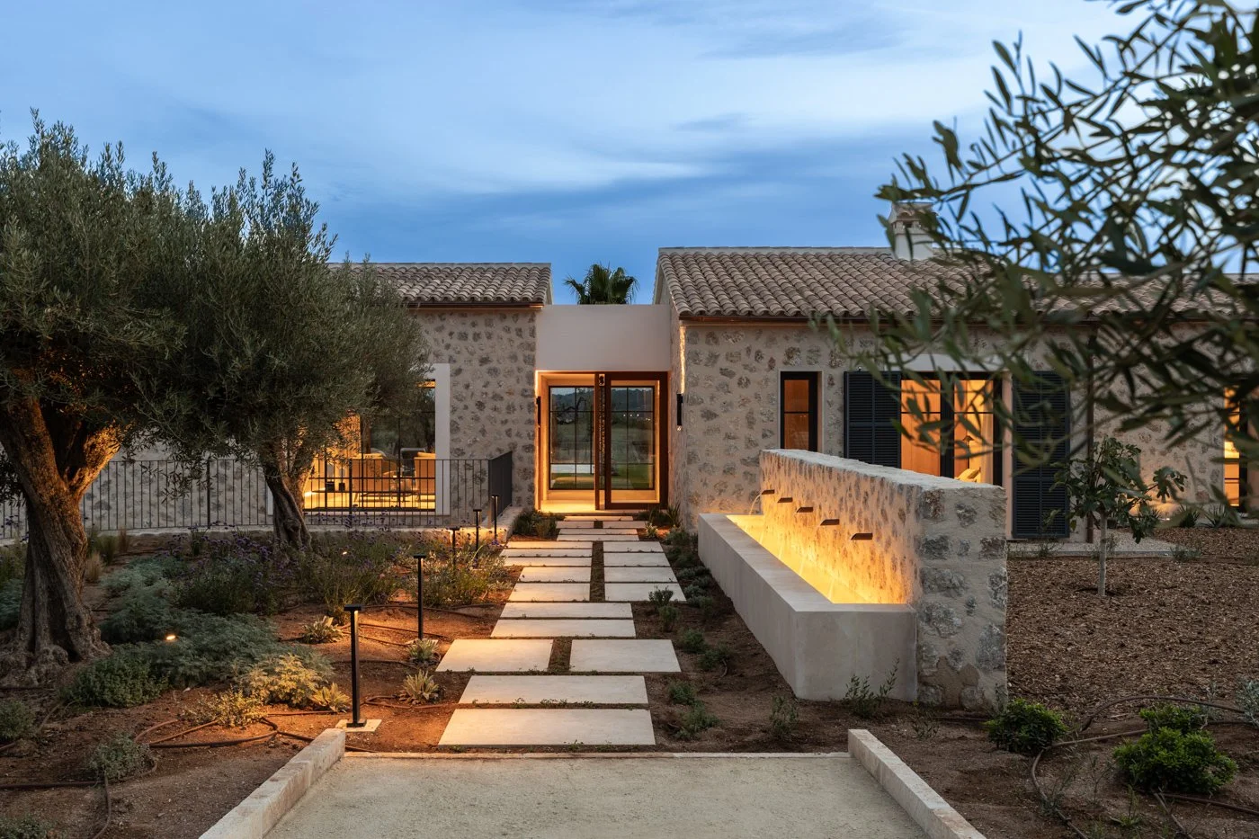 Casa moderna de piedra con jardín y camino de piedras iluminado en el atardecer