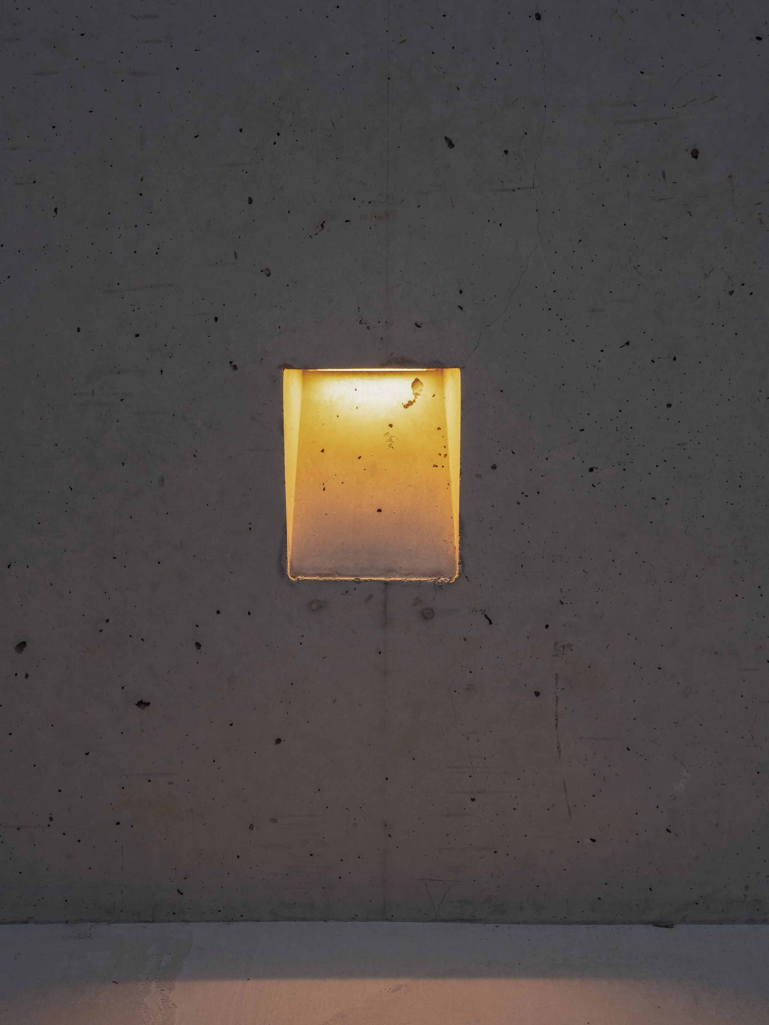 Superficie de concreto gris con un nicho iluminado en la parte central, con puntos y manchas en la superficie.