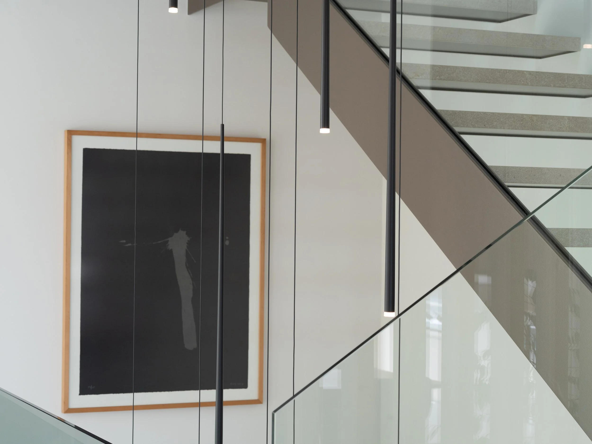 Vista de un interior moderno con una escaleras de metal y vidrio, cuadros en la pared, y un suelo brillante.