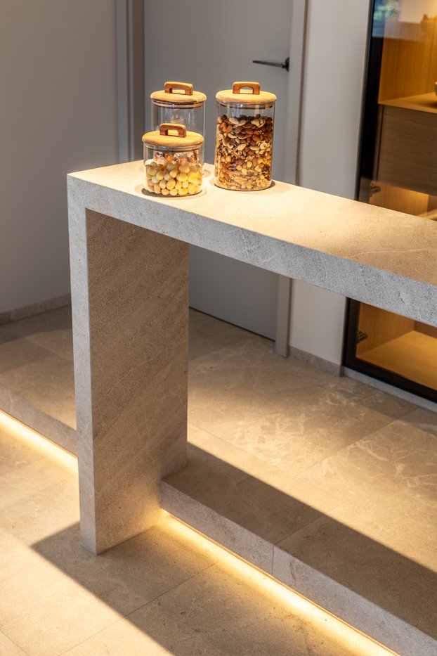 Tres frascos de vidrio con tapas de madera, llenos de dulces y cereales, sobre una mesa de piedra en un interior moderno.