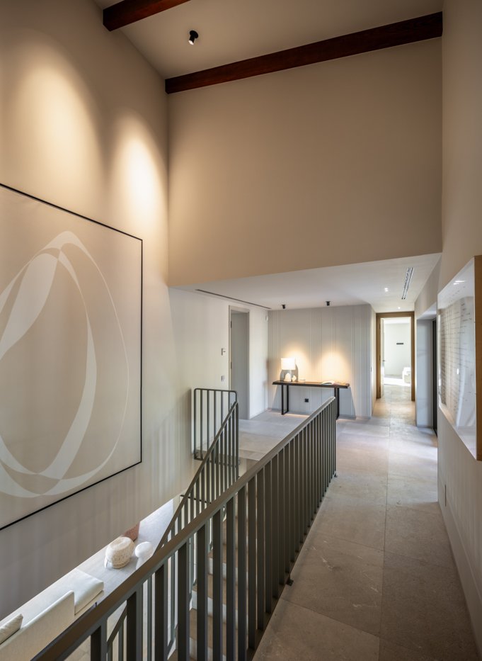 Pasillo interior en una casa moderna con paredes blancas, lámparas de luz suave, mobiliario minimalista y detalles decorativos sencillos.