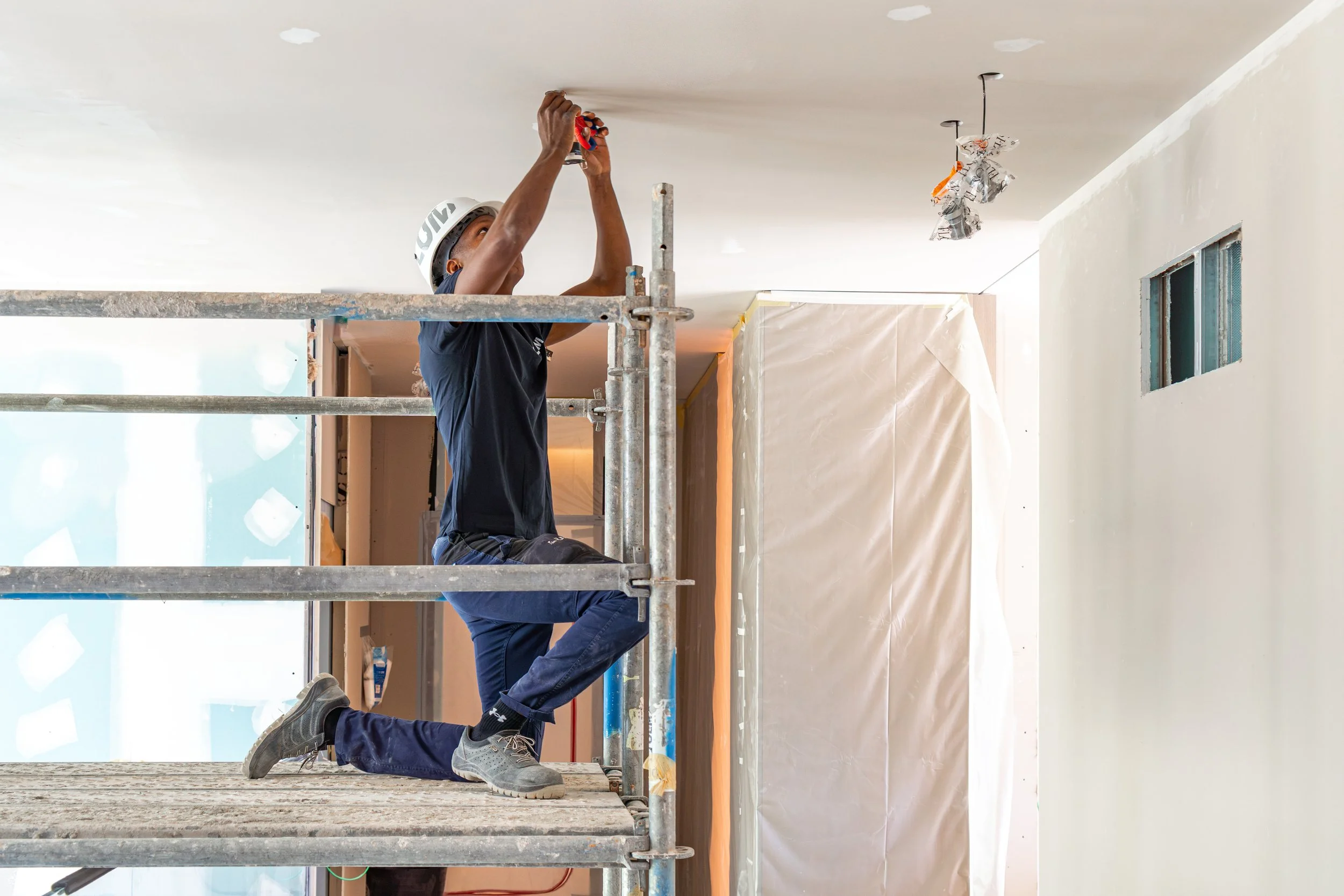 Trabajador en un andamio pintando el techo de una habitación interior.