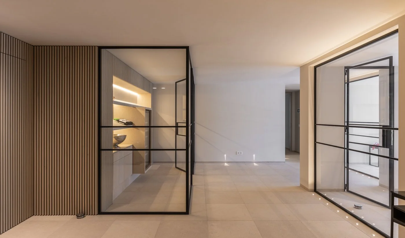 Interiores modernos con paredes de madera y marcos de puertas y ventanas de metal negro, pisos claros y luz cálida.