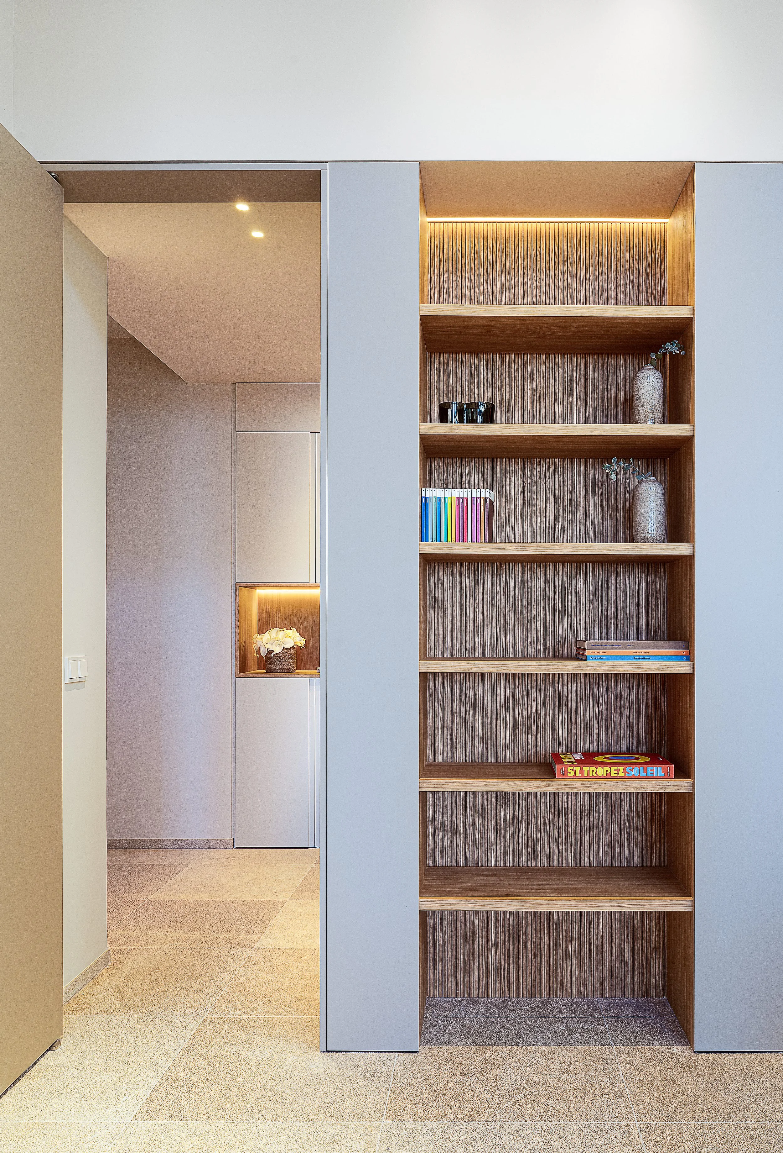 Estantería de madera con varias baldas, decorada con libros, jarrones y plantas, y revestida con madera con textura vertical.