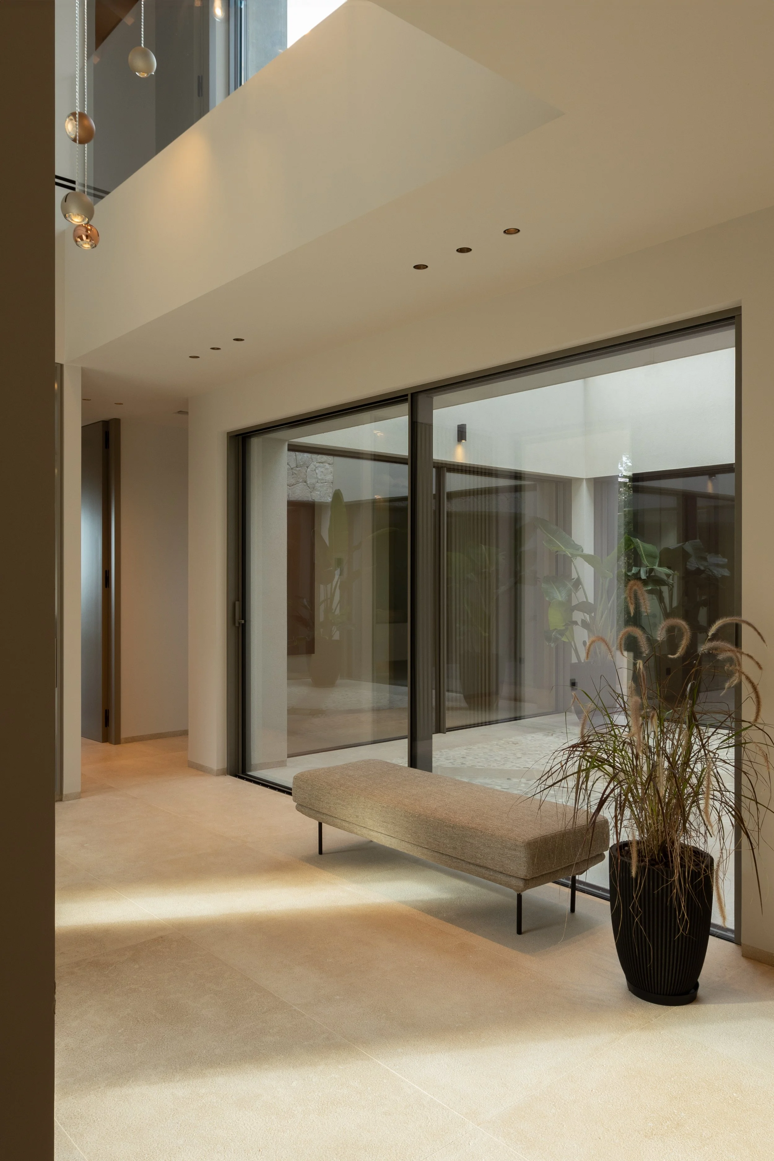 Interior moderno con ventanales grandes, planta en maceta y banco. Iluminación natural y diseño minimalista.