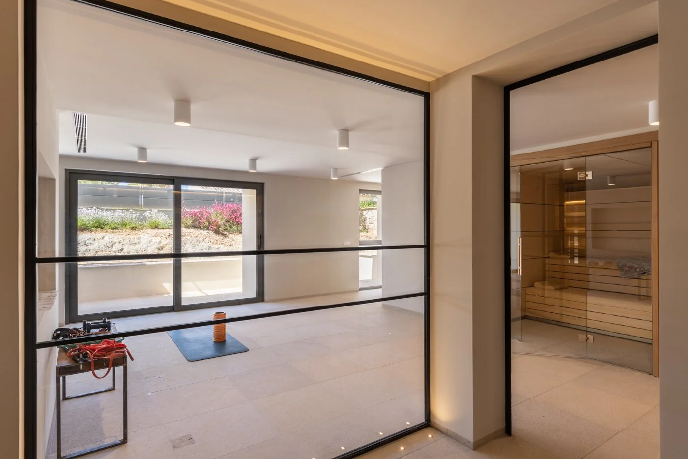 Sala de bienestar con sauna de madera y espacio para ejercicio con vista al jardín exterior.