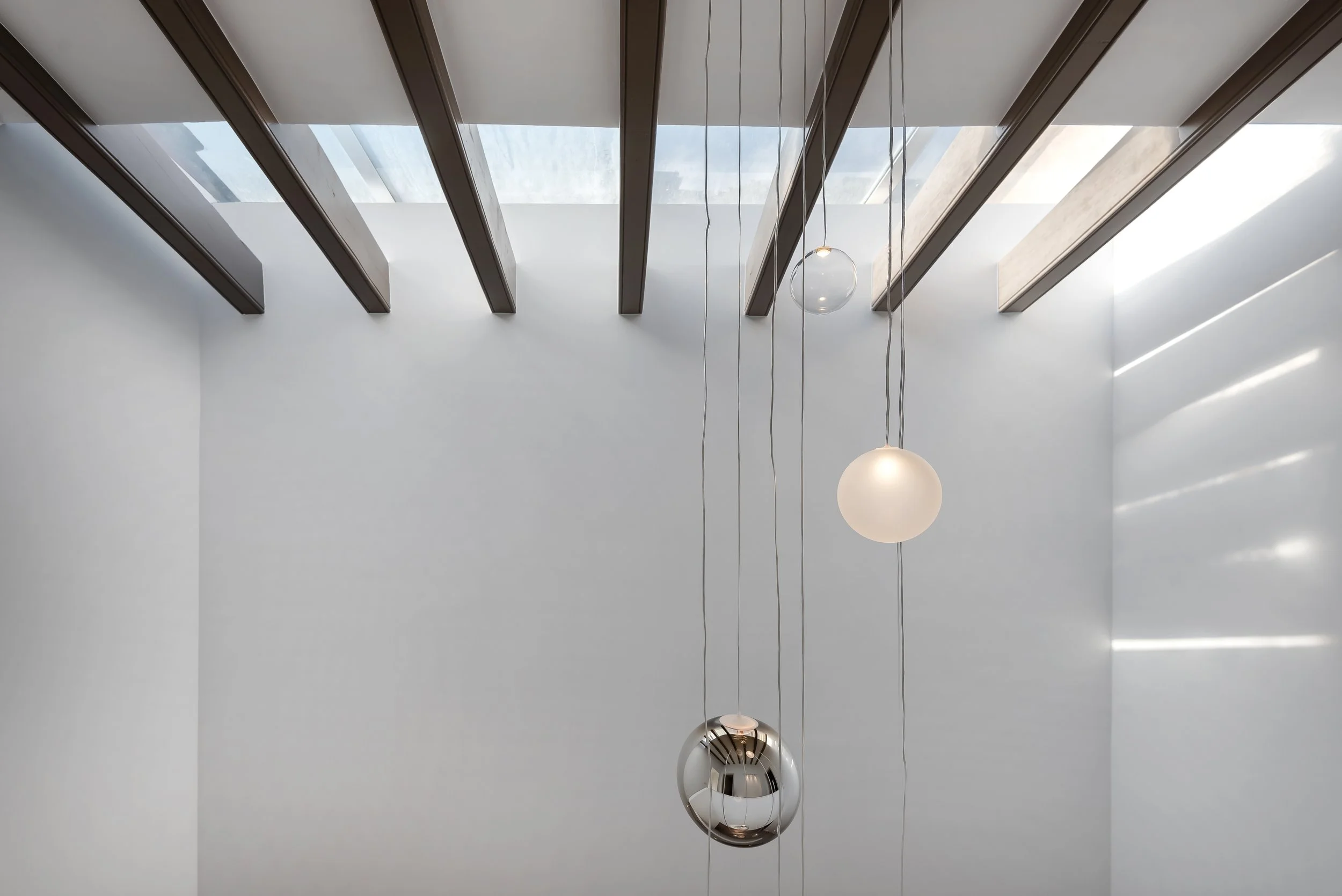 Techo con vigas de madera, lámparas colgantes de diferentes tamaños y una ventana en el techo que deja entrar luz natural.