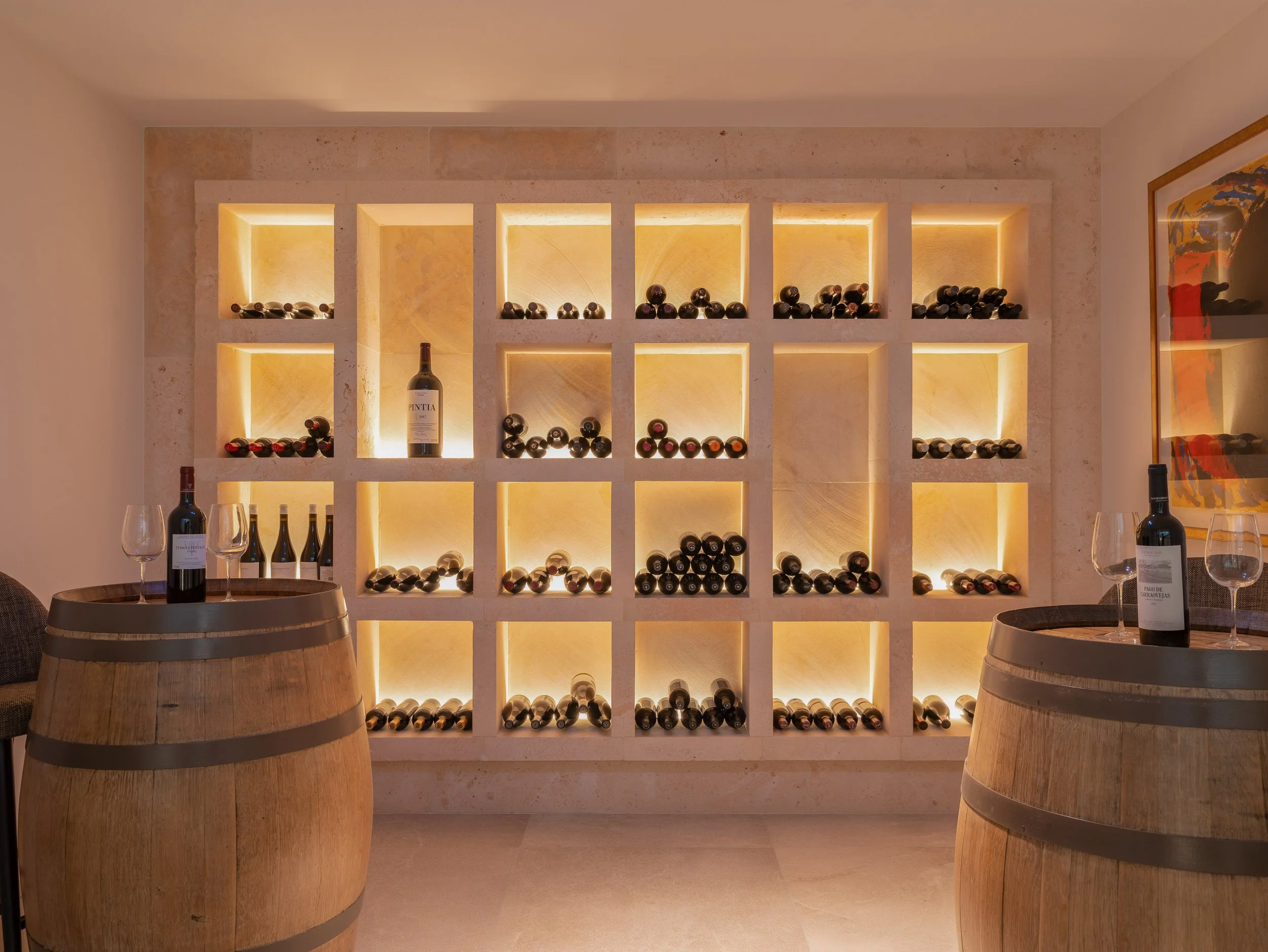 Estante con botellas de vino en un restaurante, con mesas y copas de vino en primer plano.