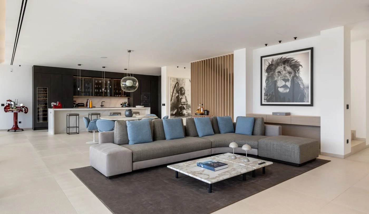 Sala de estar moderna con sofá gris y cojines azules, mesa de mármol y decoraciones, cerca de la cocina en un espacio amplio y luminoso.