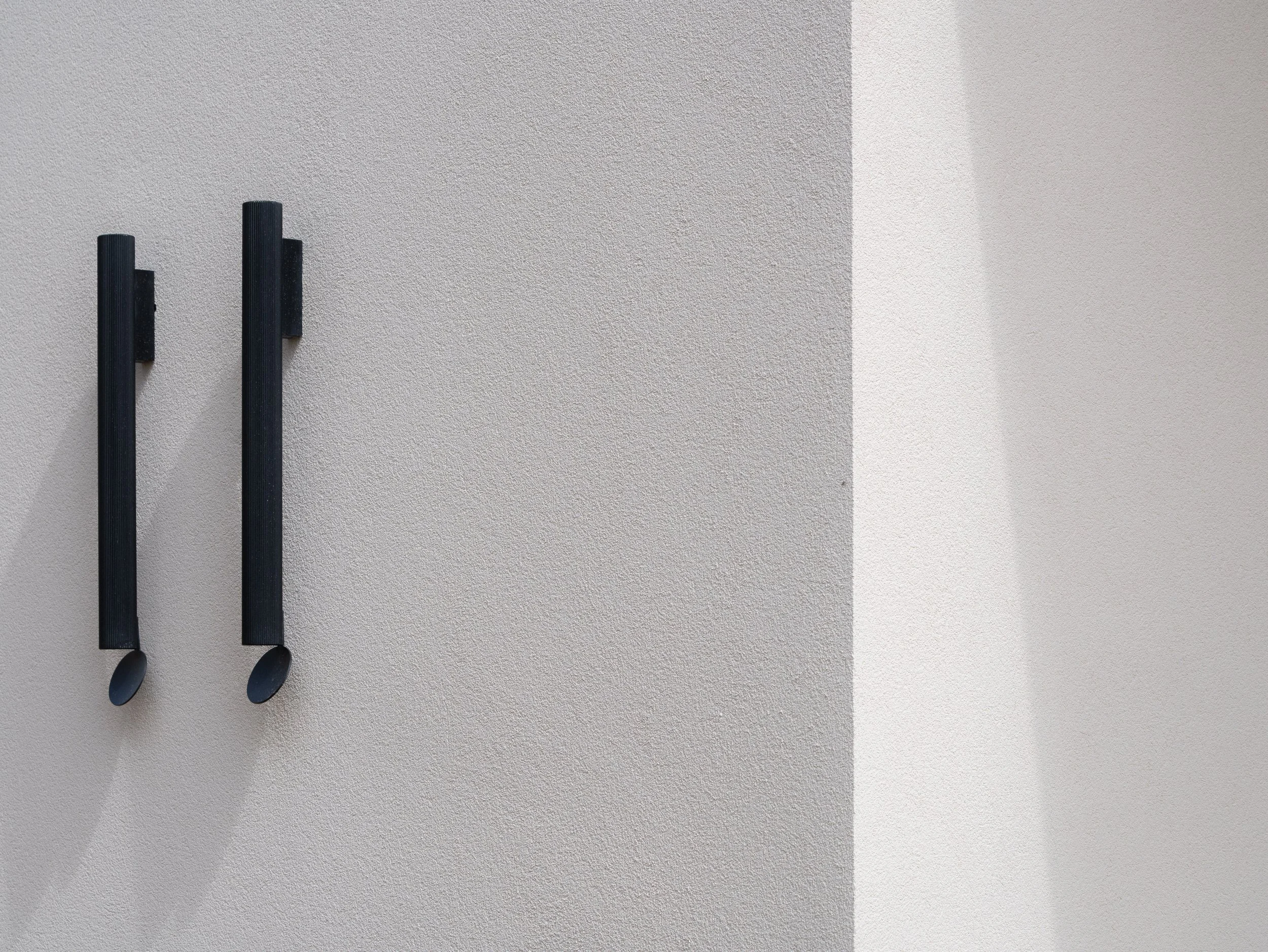 Tres siluetas de cucharas y tenedores negros colgados en una pared de color gris claro.