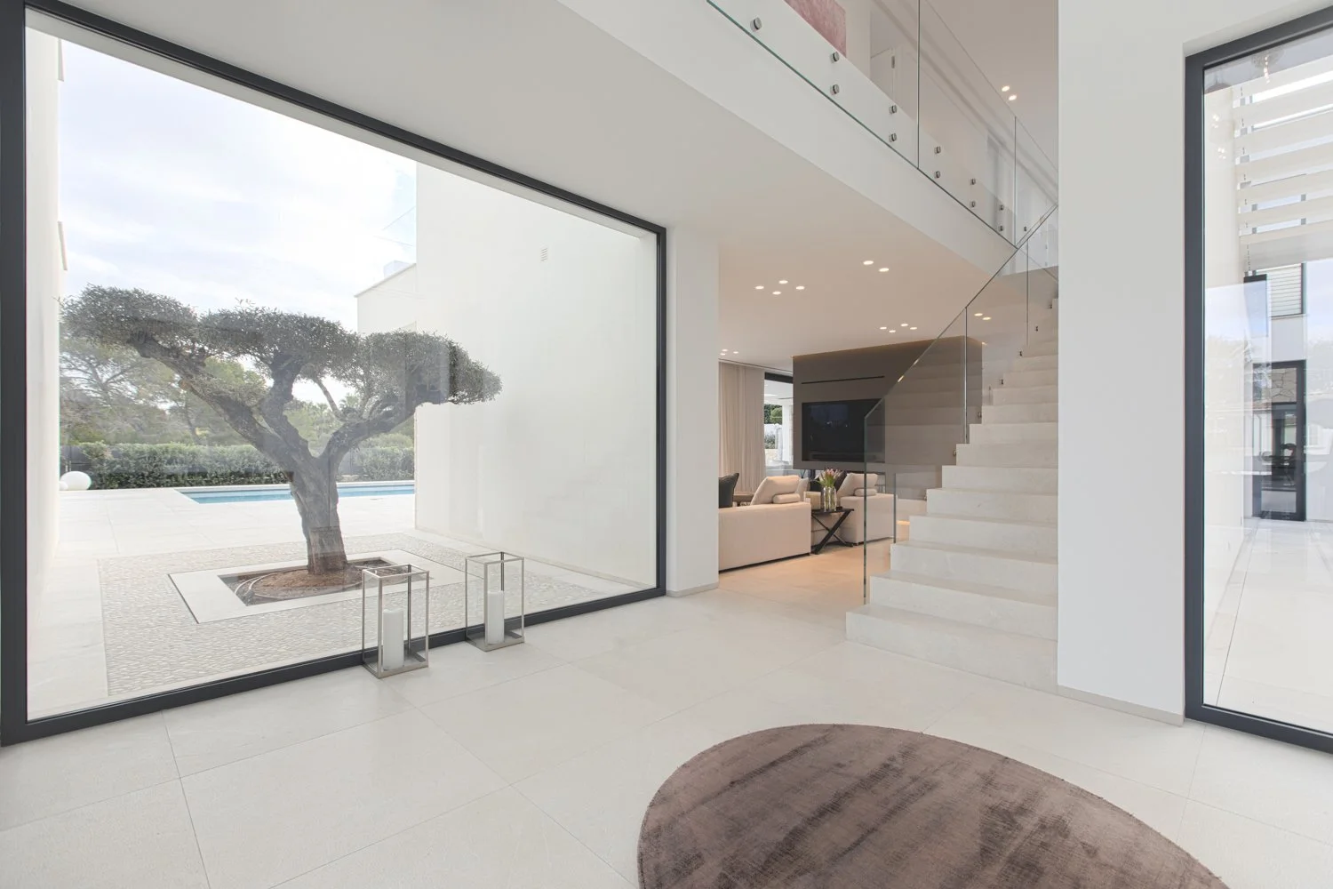 Interior de una casa moderna con vista al jardín y piscina, escaleras blancas, paredes blancas y muebles blancos.