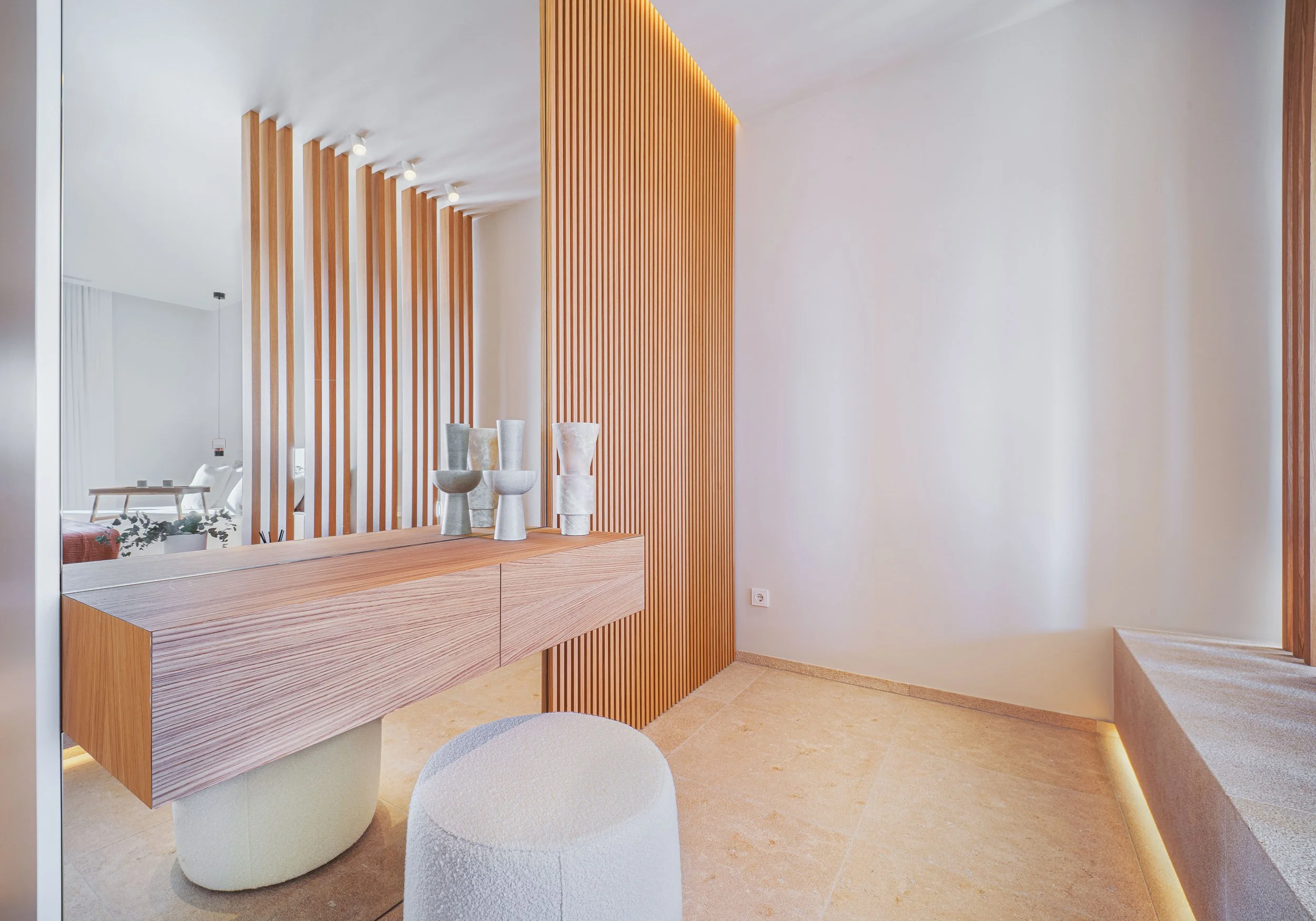 Interior de un espacio moderno con paredes blancas y paneles de madera, una mesa de madera y sillas de diseño contemporáneo, decoradas con jarrones de piedra y plantas.
