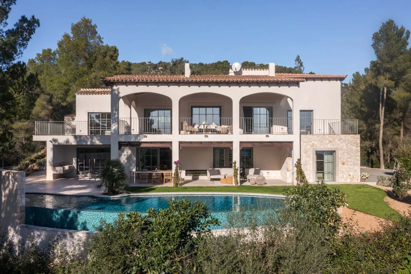 Casa moderna de dos pisos con terraza, piscina y jardín, rodeada de árboles y naturaleza.