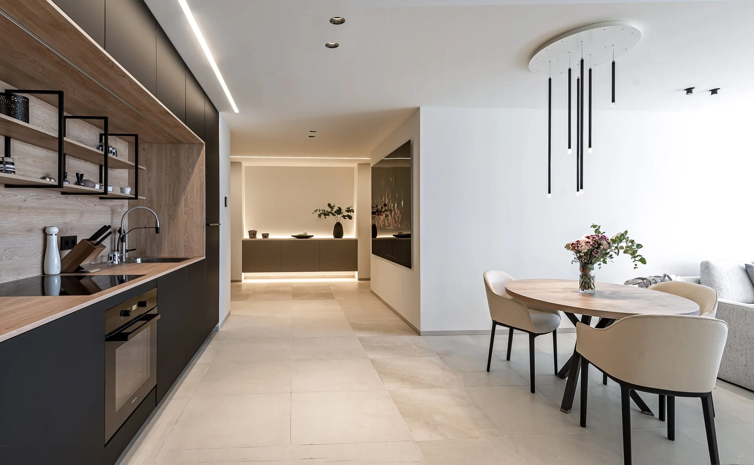 Interiores modernos de una sala y cocina con muebles de madera y paredes blancas, incluyendo una mesa redonda con sillas y una decoración minimalista.