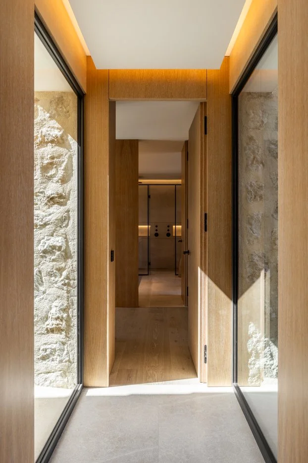 Entrada a un pasillo en un interior con paredes de piedra y puertas de madera.