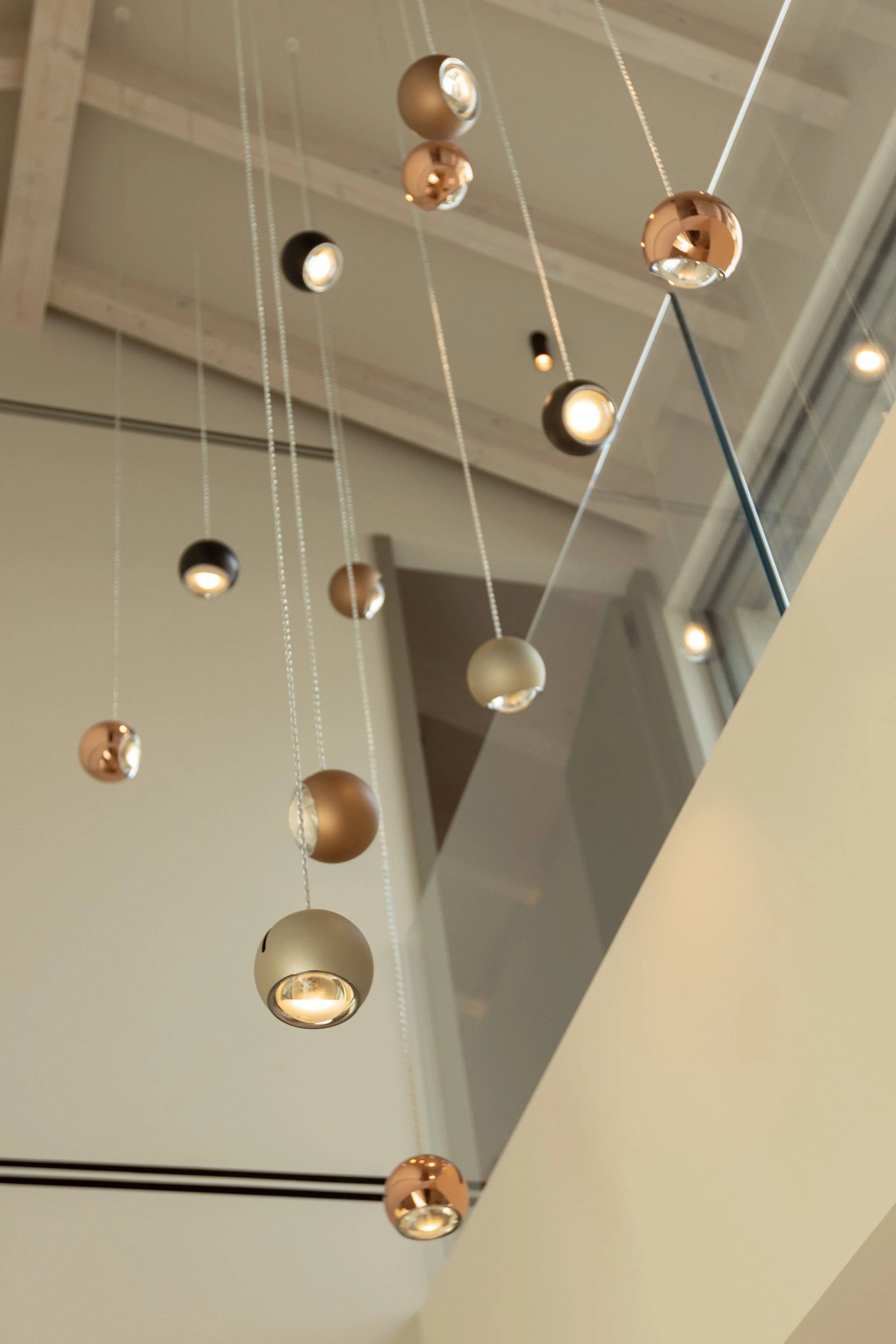 Lámpara moderna con esferas metálicas suspendidas en cables en una pared de fondo en blanco y techo de madera.