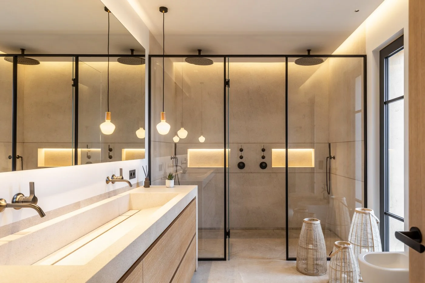 Baño moderno con doble lavabo, espejos grandes, paredes de piedra, ducha con puertas de vidrio negro y varias lámparas colgantes