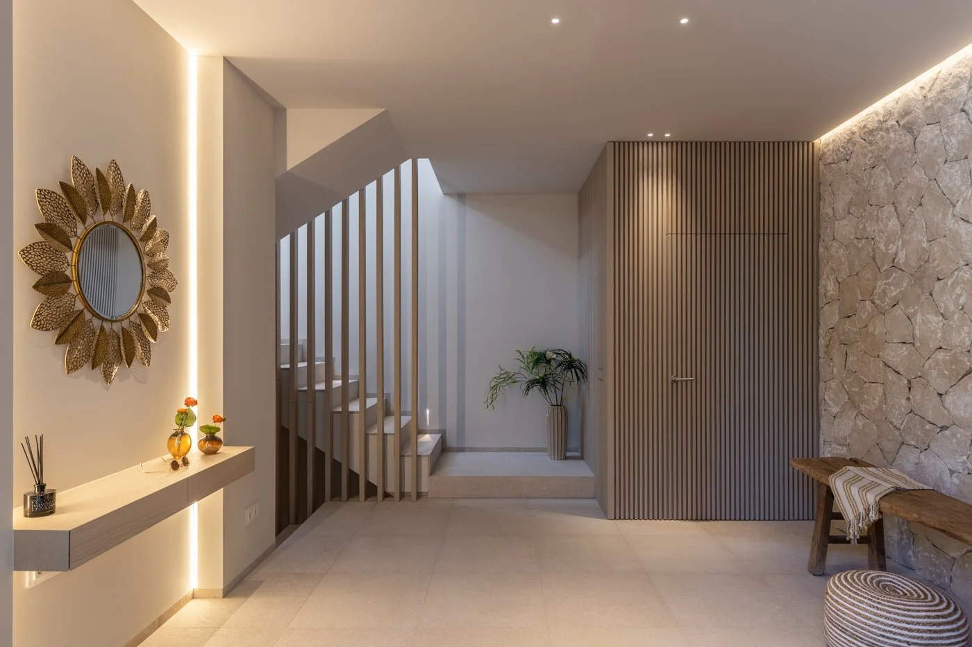 Entrada moderna con paredes de piedra y madera, escaleras, plantas y un espejo decorativo.