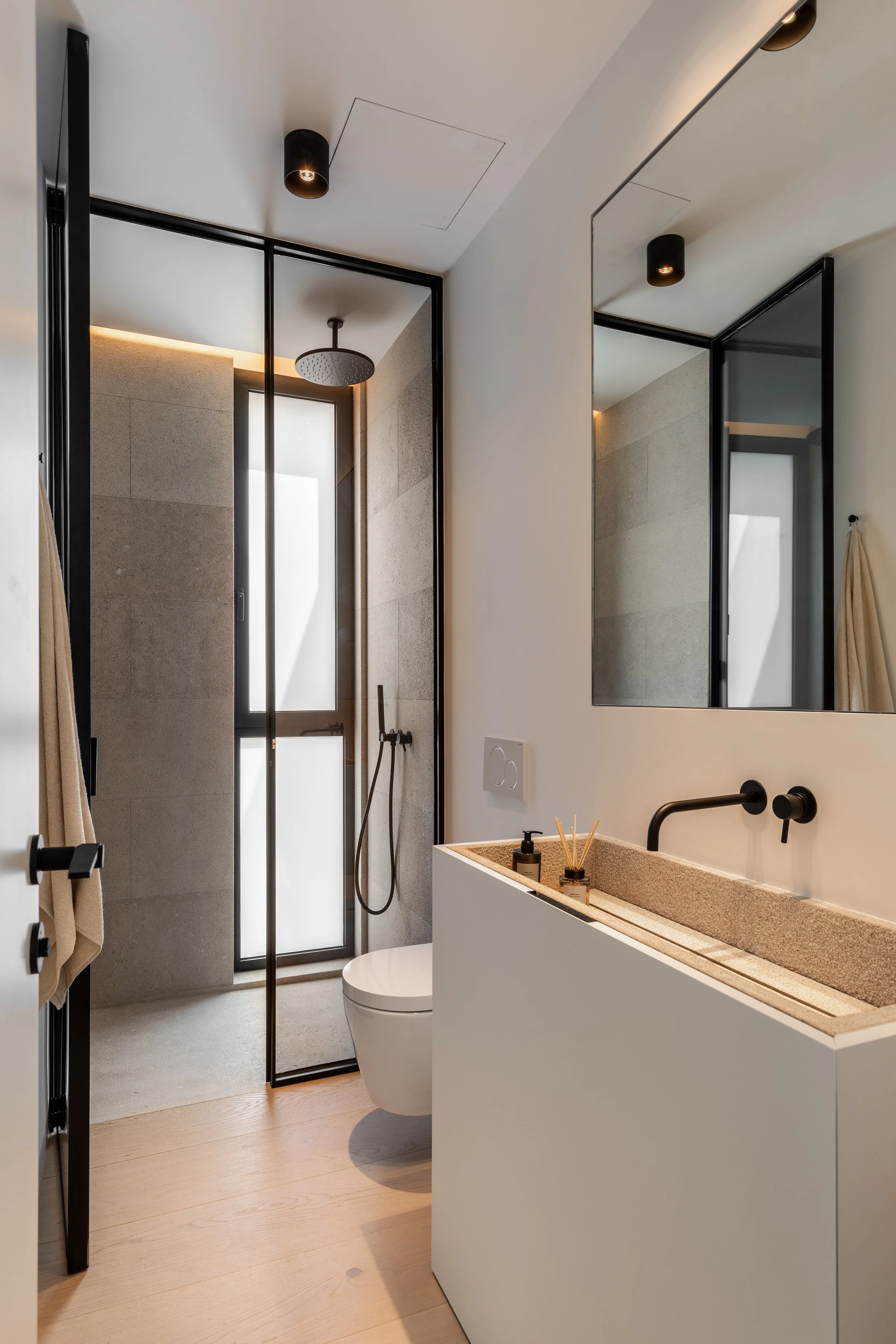 Baño moderno con ducha, lavabo y espejo grande, decorado en tonos neutros y con accesorios en negro.