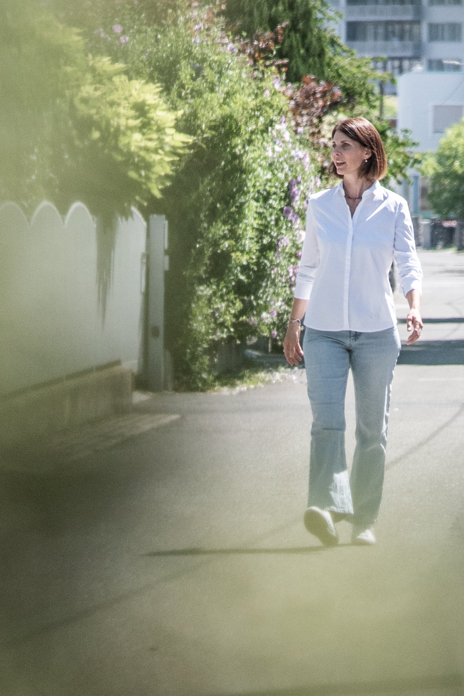 Eine Frau geht an einem sonnigen Tag an einer begrünten Straße vorbei.