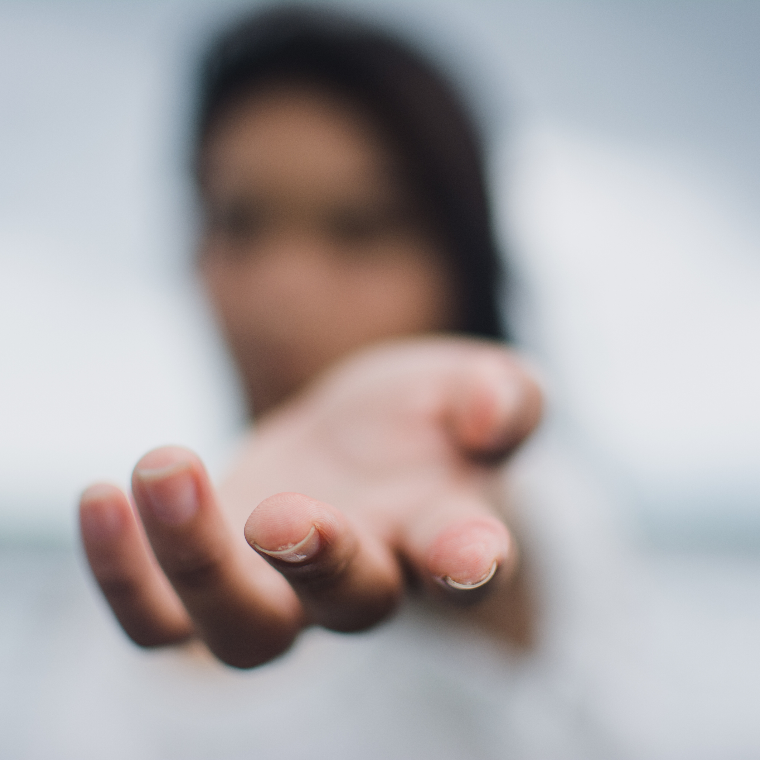 Close-up of a hand with fingers touching a reflective surface, with a blurred background.