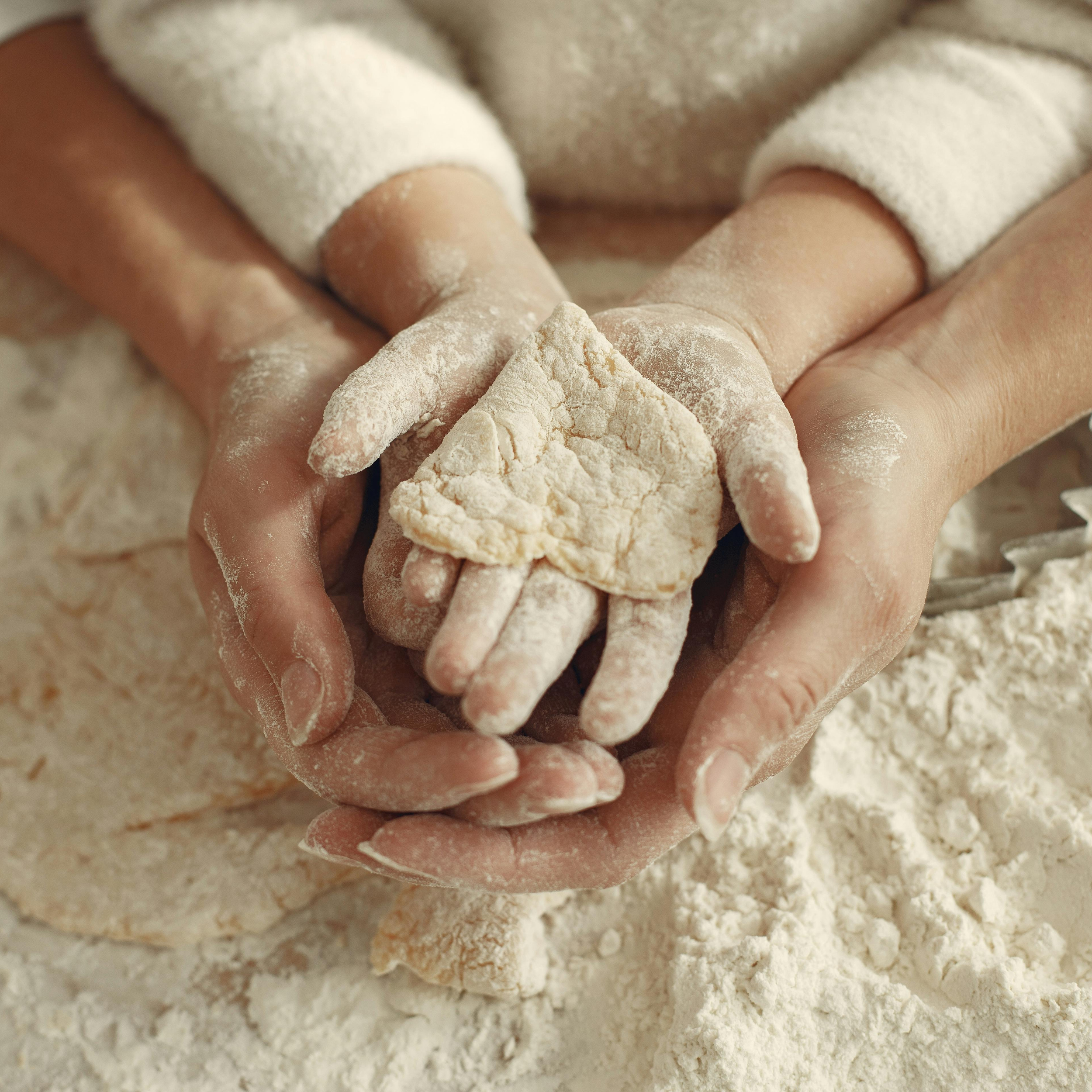 Close-up of hands covered in flour, preparing to make dough with flour and dough pieces.