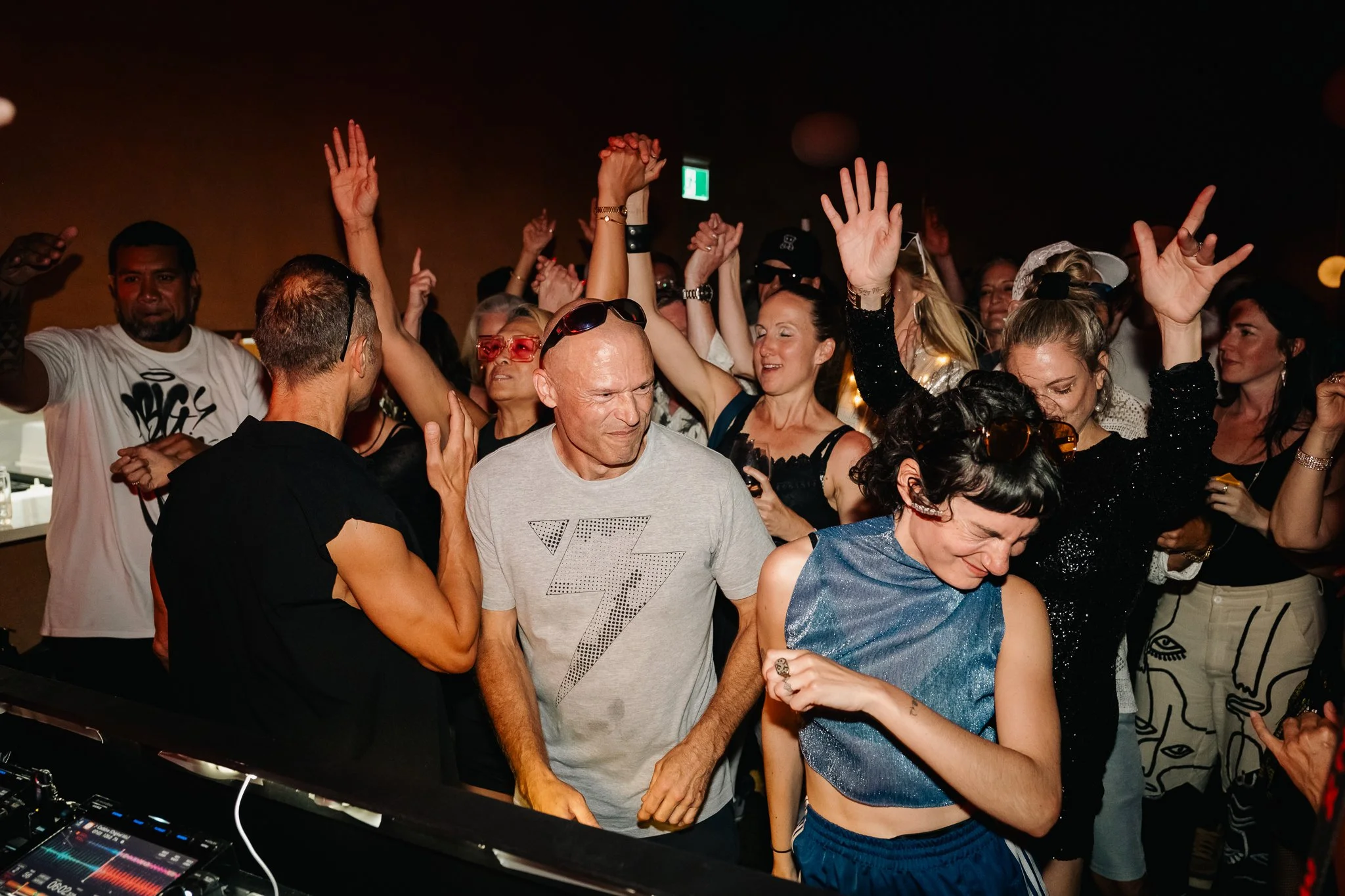 Crowd of people dancing and enjoying a night out at a club or party, with some raising their hands and smiling.