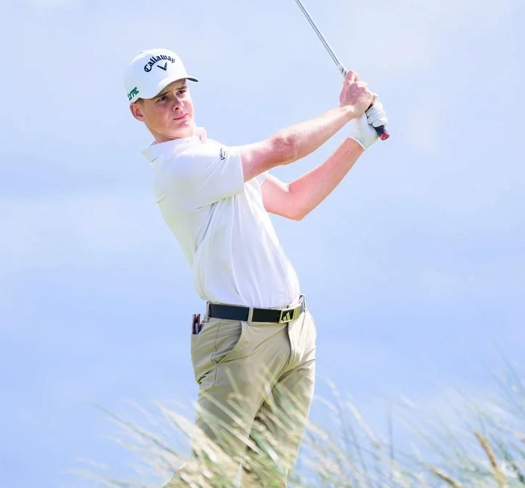 Young male golfer in white shirt and beige pants swings a golf club outdoors.