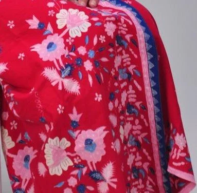 Close-up of a red fabric with floral embroidery and a border, possibly part of a garment or textile item.