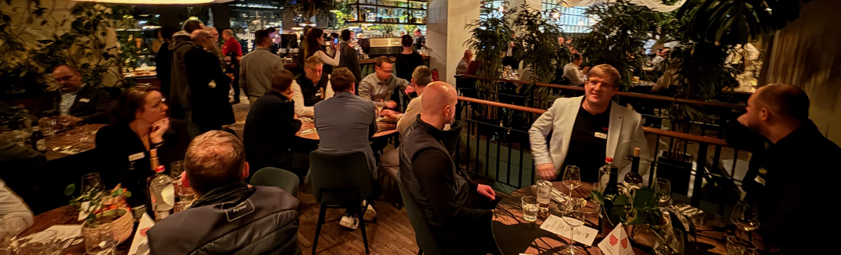 Een druk restaurant met mensen die genieten van een maaltijd en conversatie, tafel gevuld met glazen, borden en decoraties.