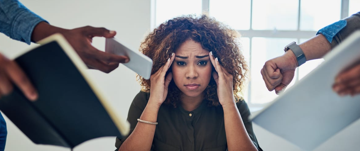 Woman with curly hair holding her head in frustration while being overwhelmed by multiple hands offering documents and a phone.