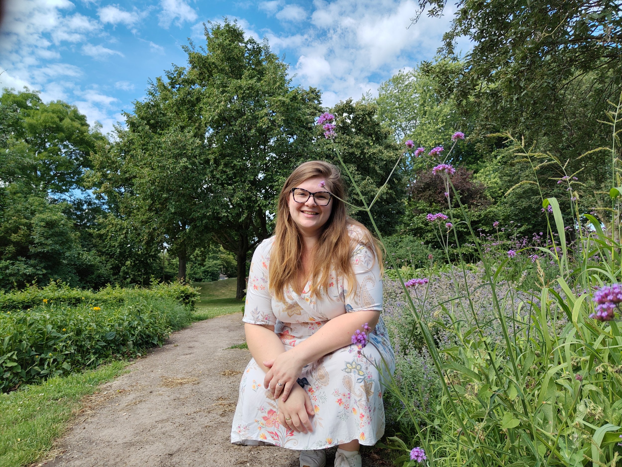 Laura zit gehurkt langs een wandelpad met paarse bloemen