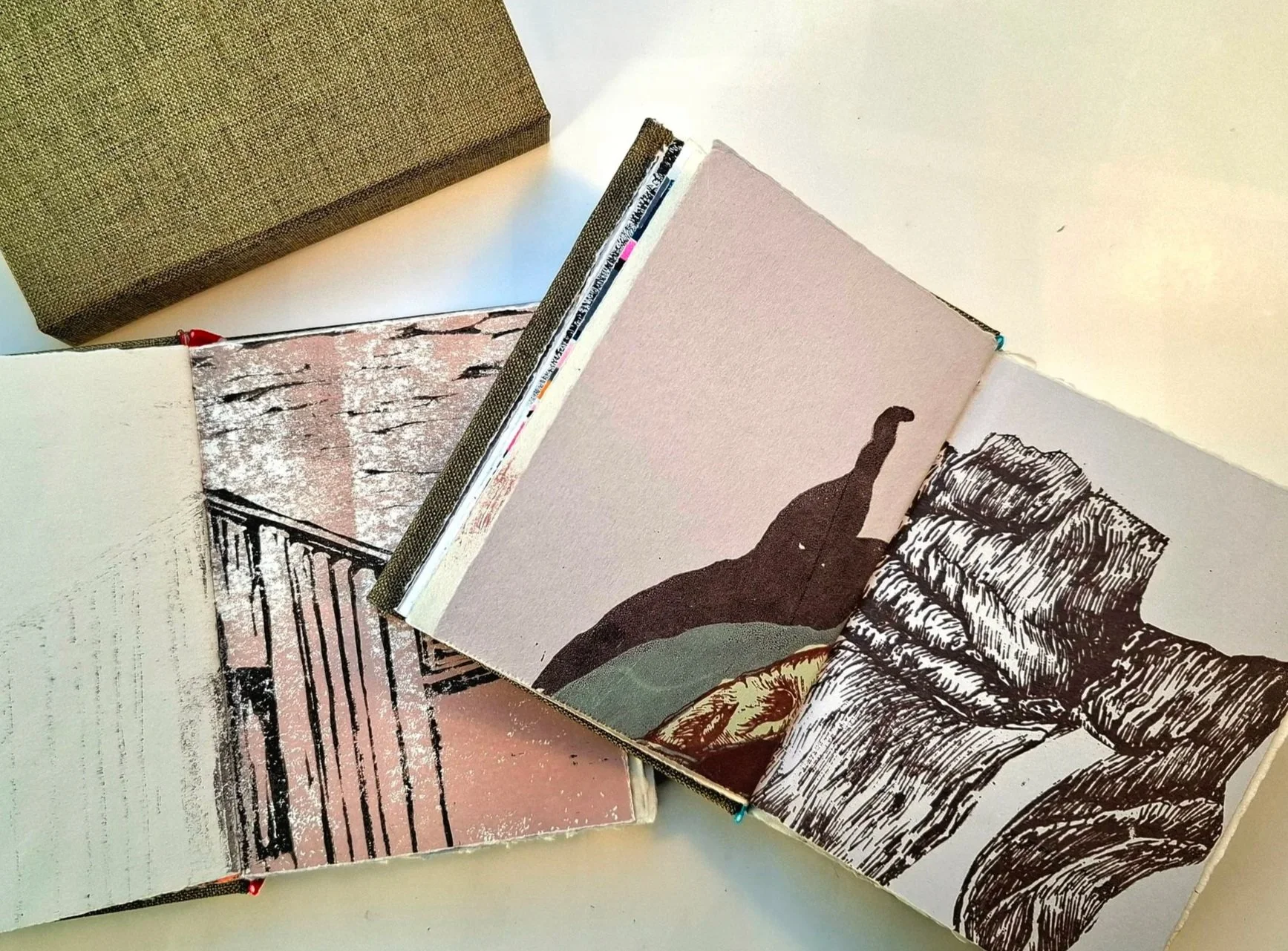 Open art book showing black and white illustrations of a landscape with mountains, trees, and a person walking along a trail.